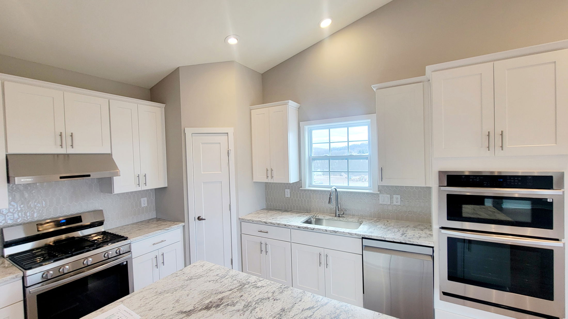 Modern kitchen with white cabinets, stainless steel appliances, and a marble countertop island under recessed lighting.