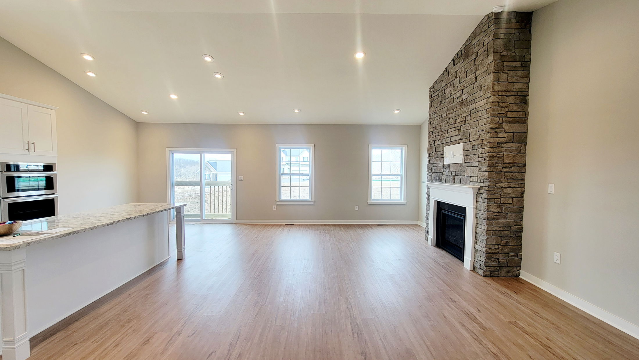Open concept living room with hardwood floors, stone fireplace, and a modern kitchen with granite countertops.