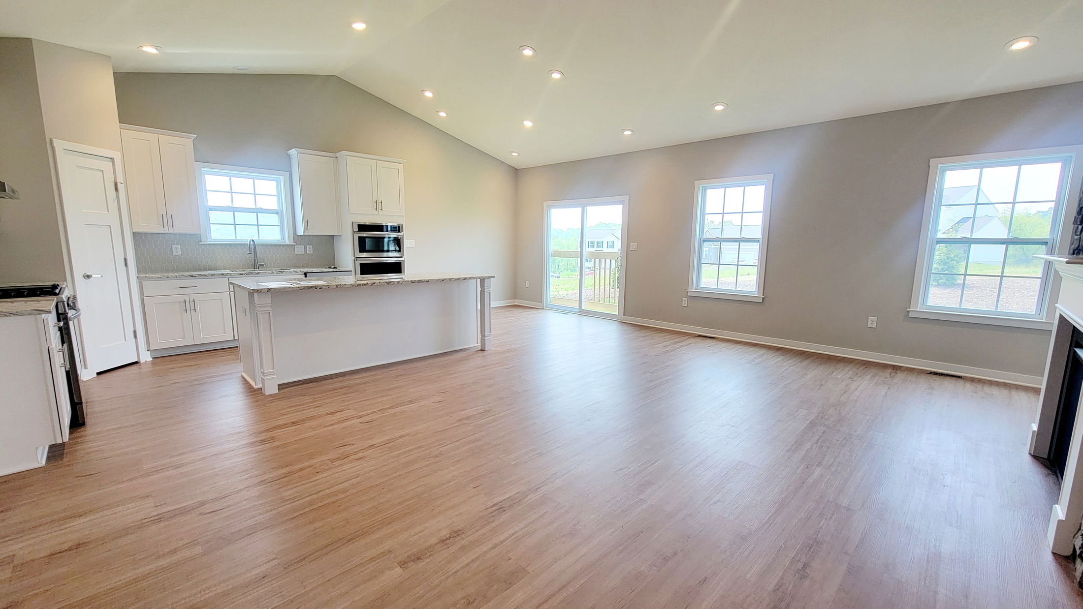Spacious modern open-concept kitchen and living room with hardwood floors, white cabinets, and ample natural light from large windows.