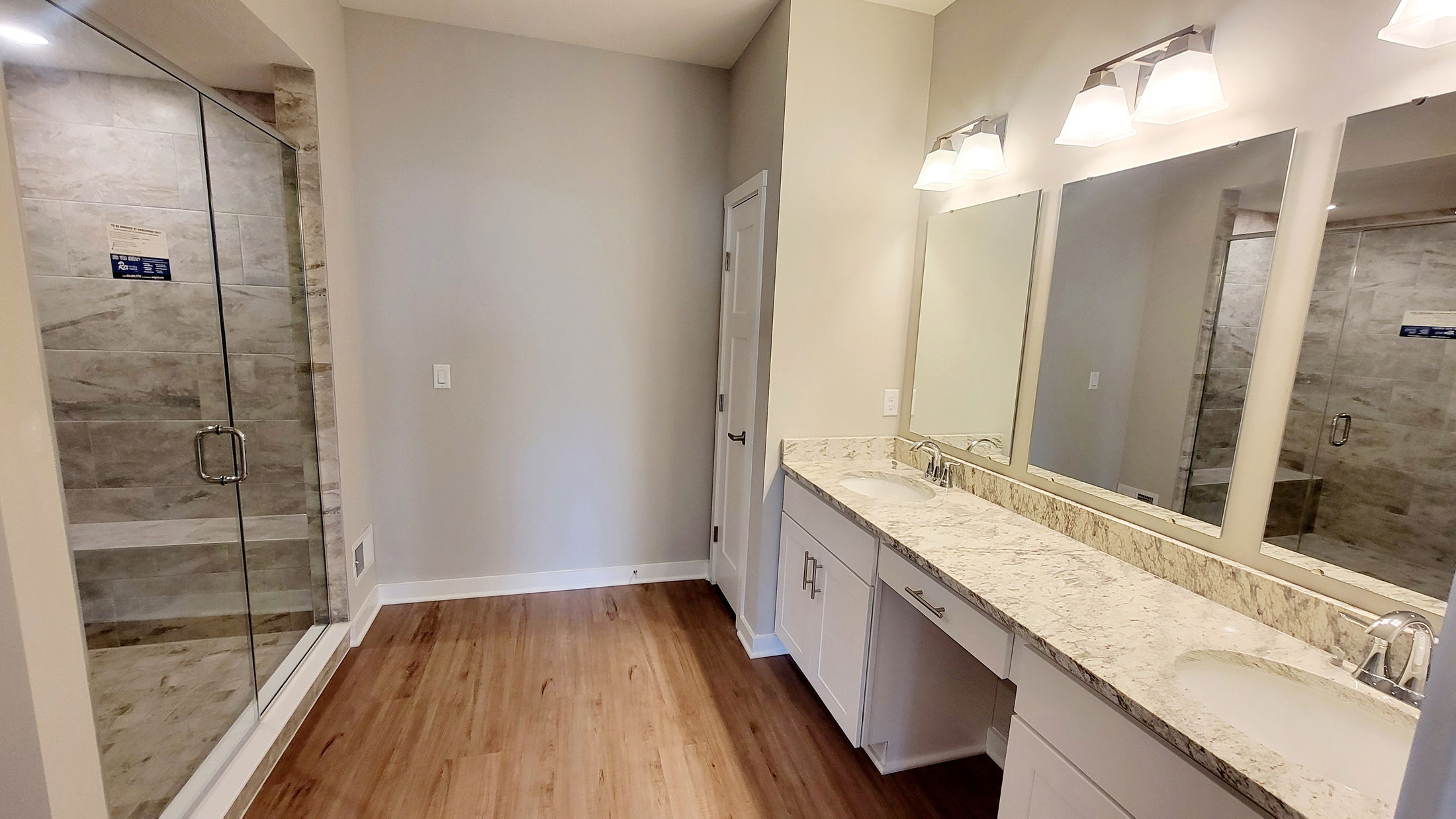 Modern bathroom with dual sinks, granite countertop, large mirrors, and a glass-enclosed tile shower.
