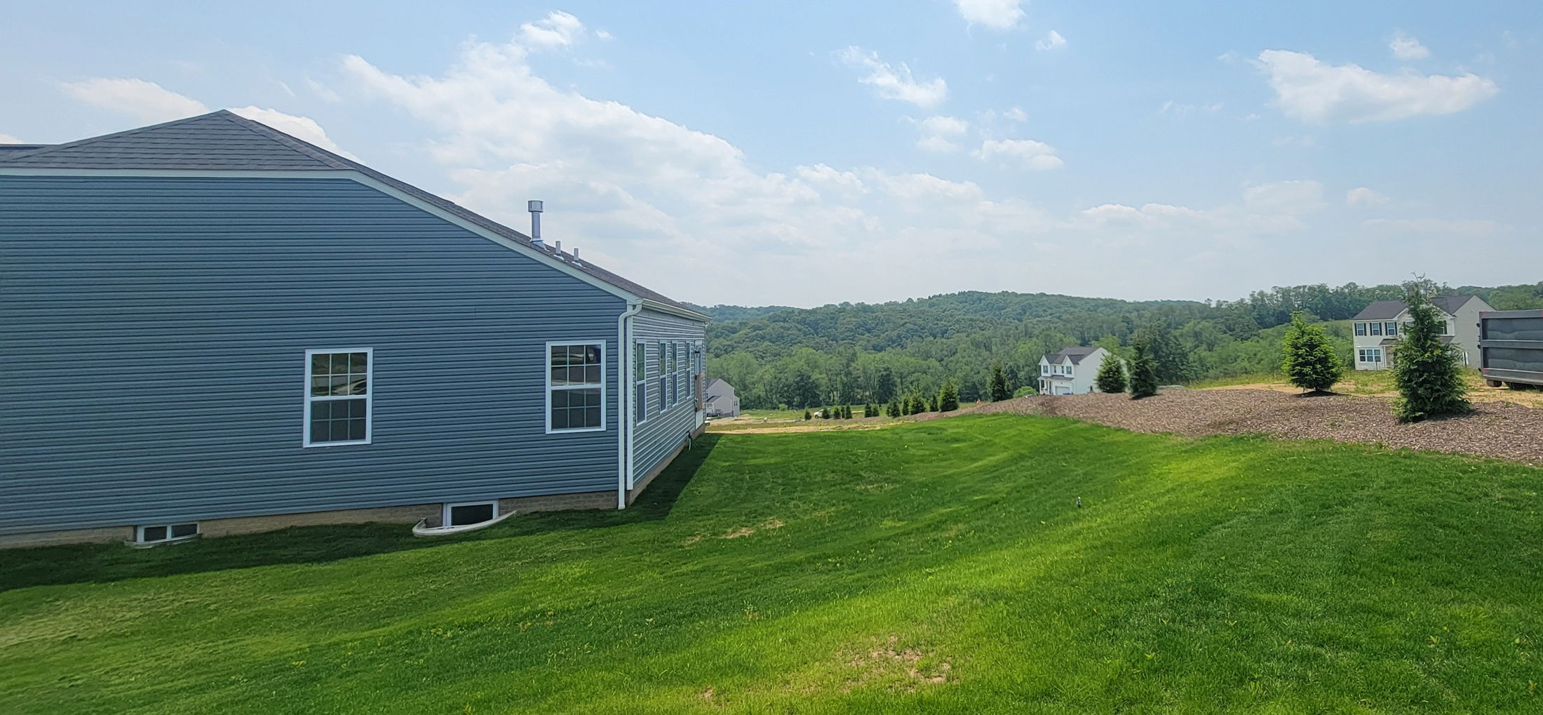 Modern blue house with white trim on a lush green lawn, set against a backdrop of distant hills and clear blue skies.