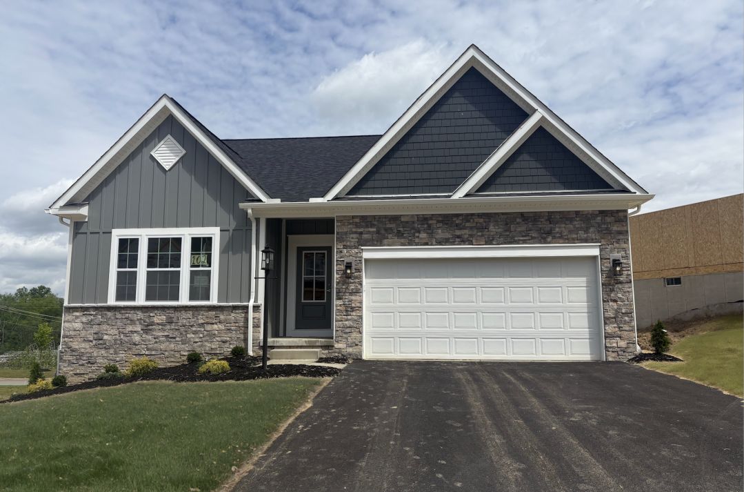 Modern suburban single-story house with gray siding, large front-facing windows, stone accents, and a white double garage door.