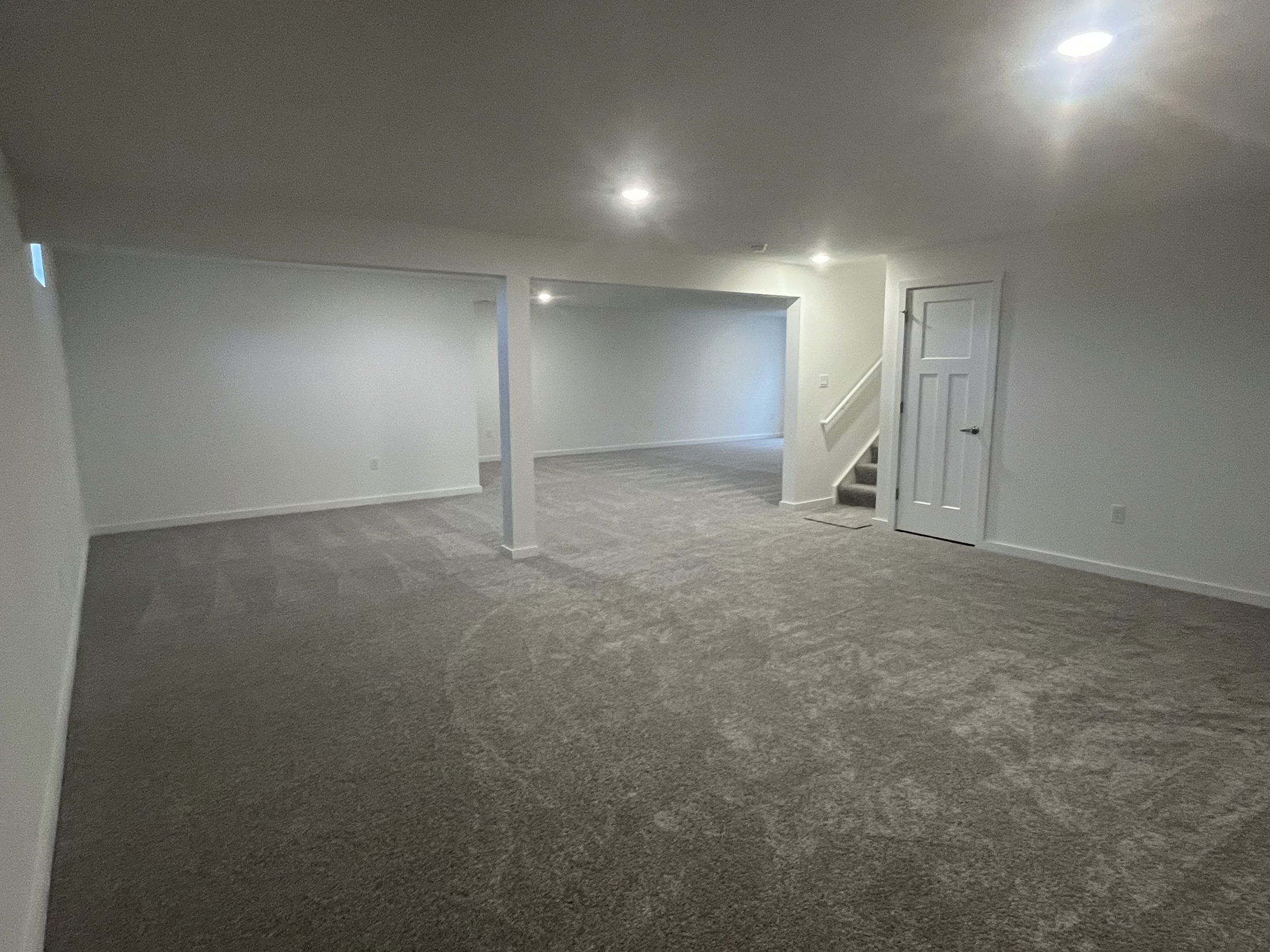 Spacious, newly renovated basement with gray carpet and recessed lighting.