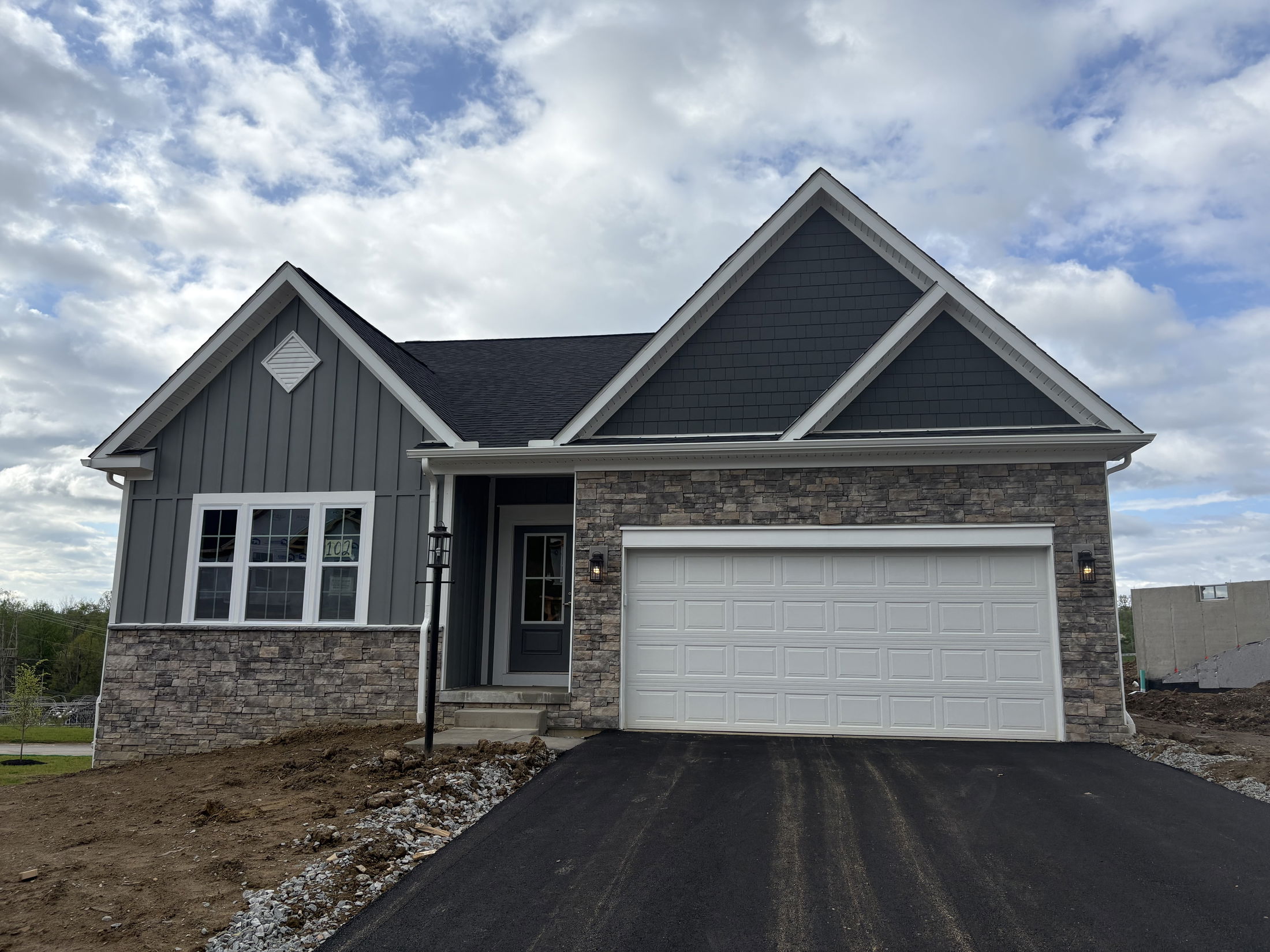 Newly constructed modern suburban home with a two-car garage and a stone façade under a cloudy sky.
