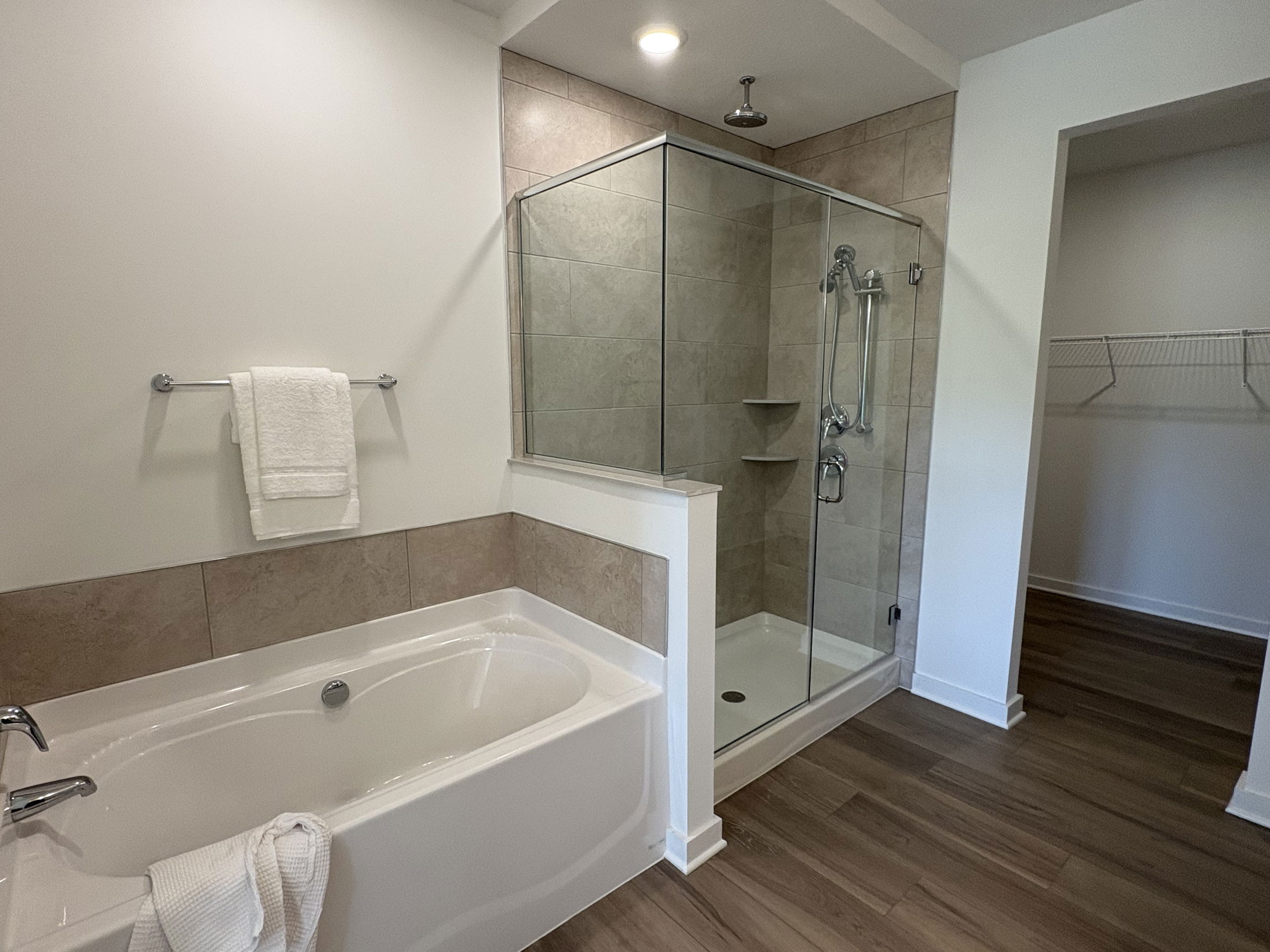 Modern bathroom featuring a glass-enclosed shower, white bathtub with towels, and wood-style flooring.