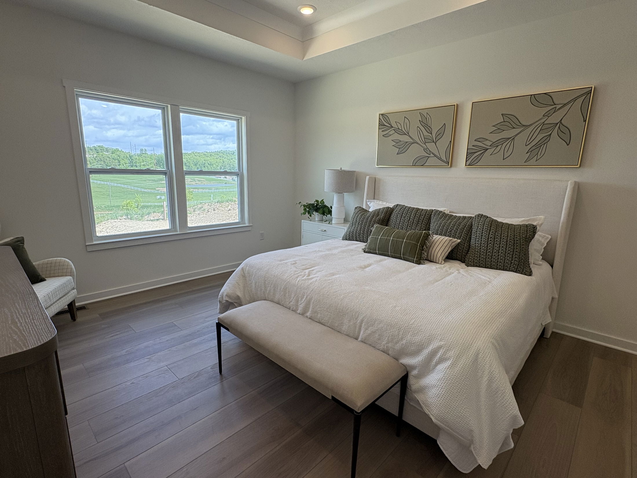 Elegant bedroom with a white bed, green pillows, and countryside view through large windows.