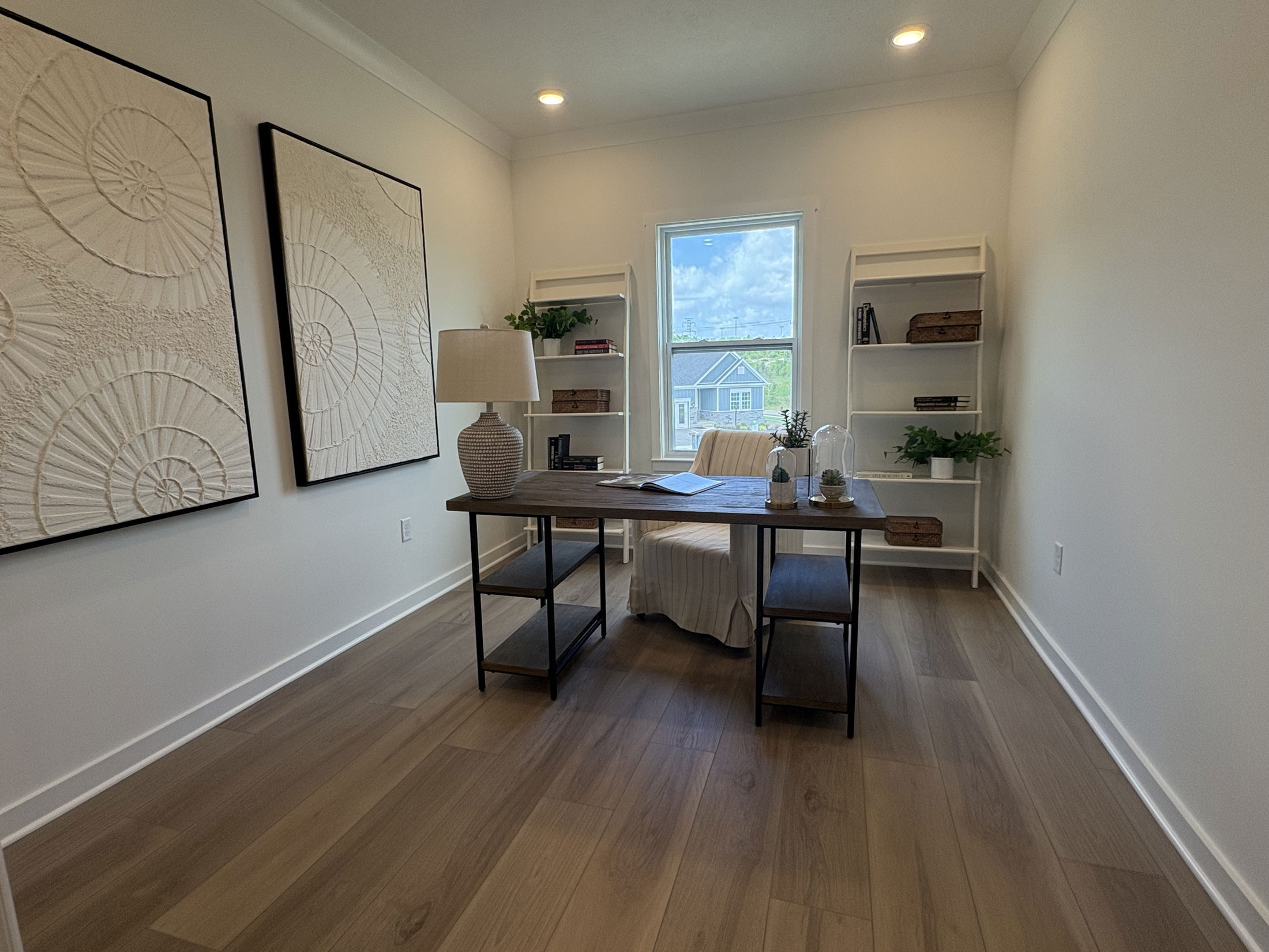Modern home office with wooden desk, decorative wall art, bookshelves, and window view.