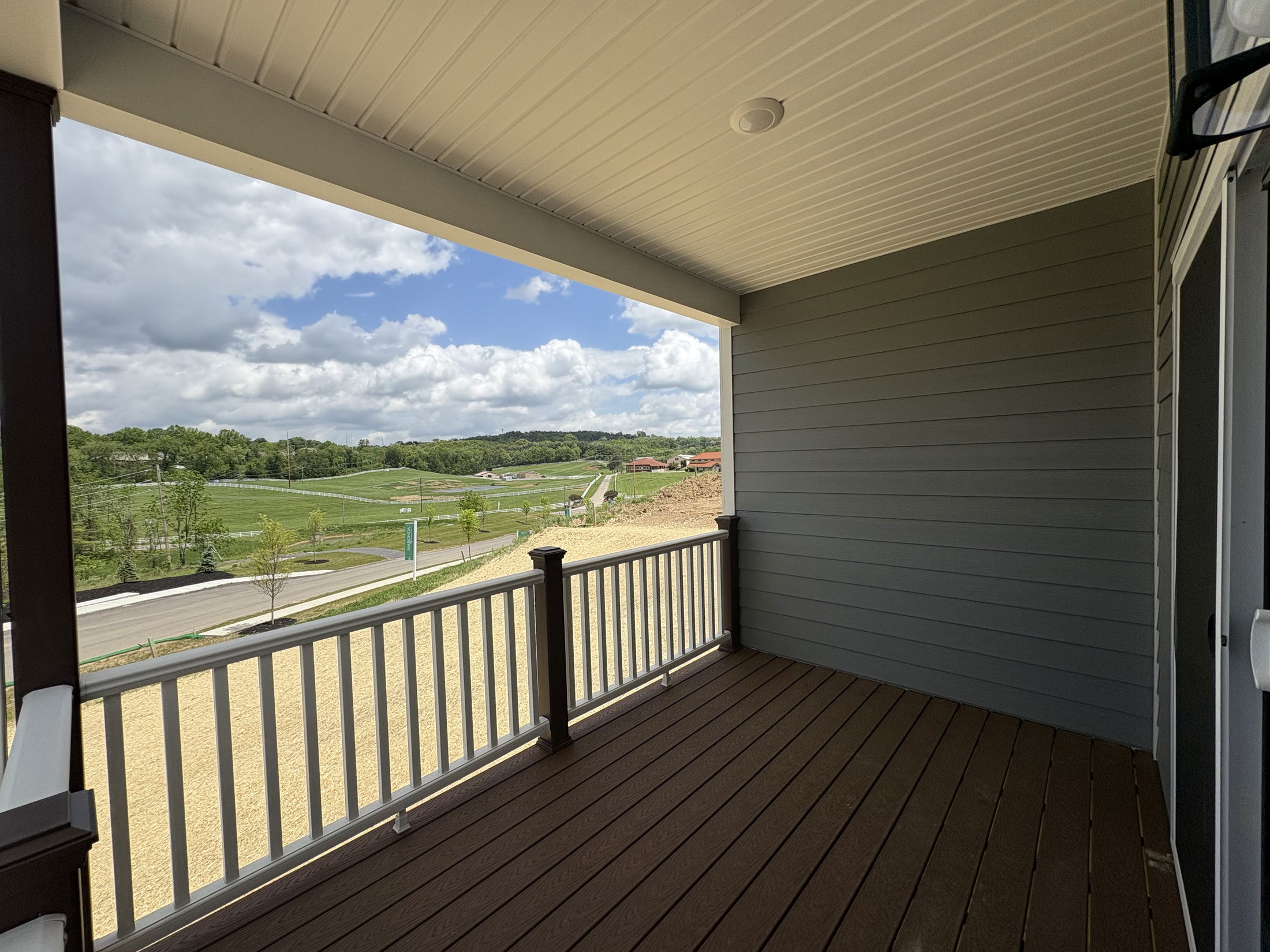 Covered balcony with wooden deck overlooking a scenic view of green fields and cloudy sky.