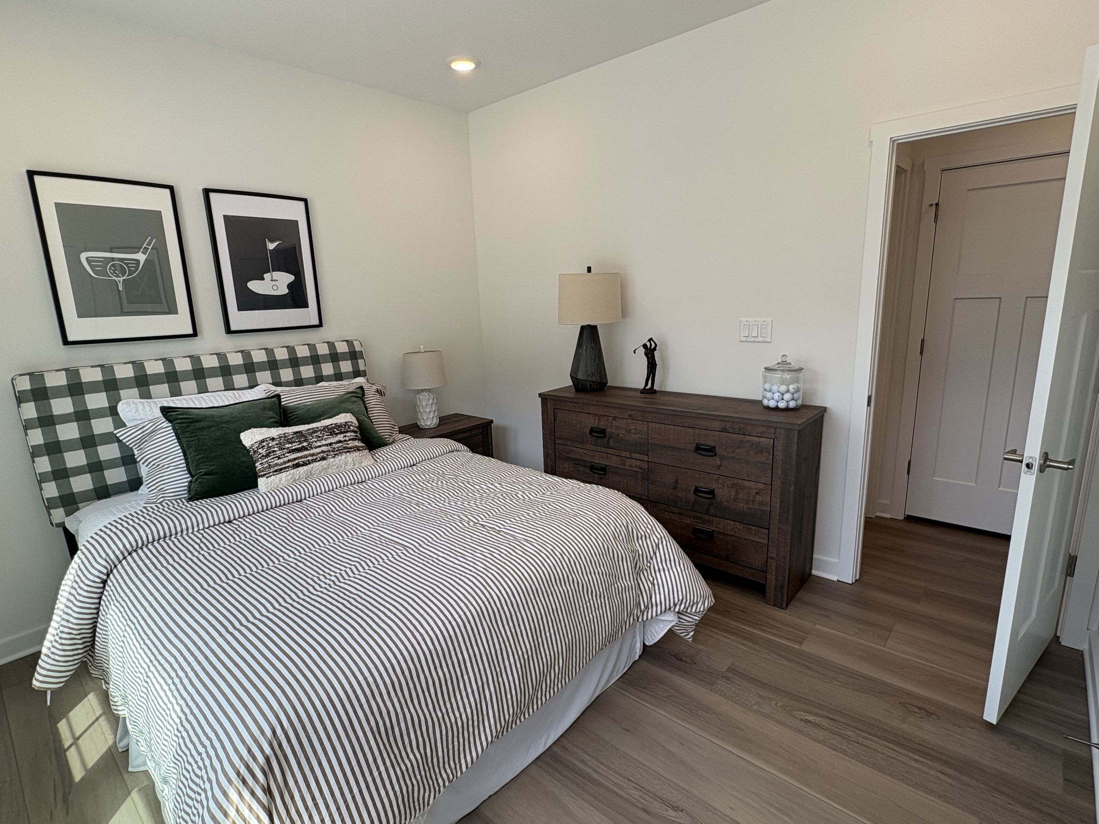 Cozy bedroom with striped bedding, plaid headboard, and modern decor featuring golf-themed artwork and a wooden dresser.