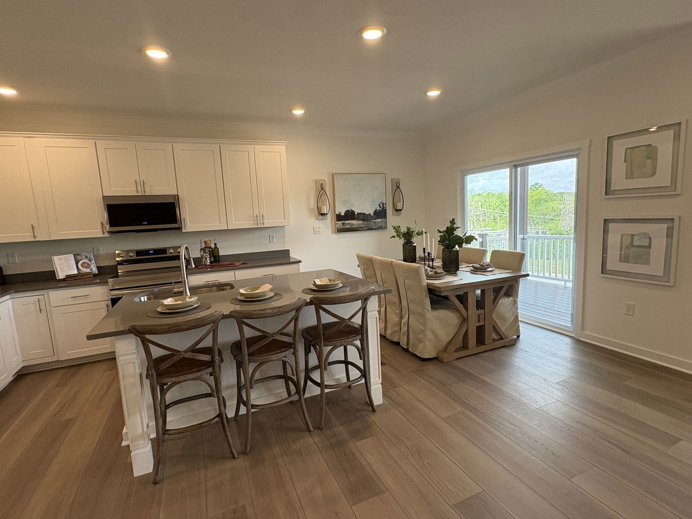 Modern kitchen and dining area with white cabinets, a gray island, wooden barstools, and a view of a green landscape through glass doors.