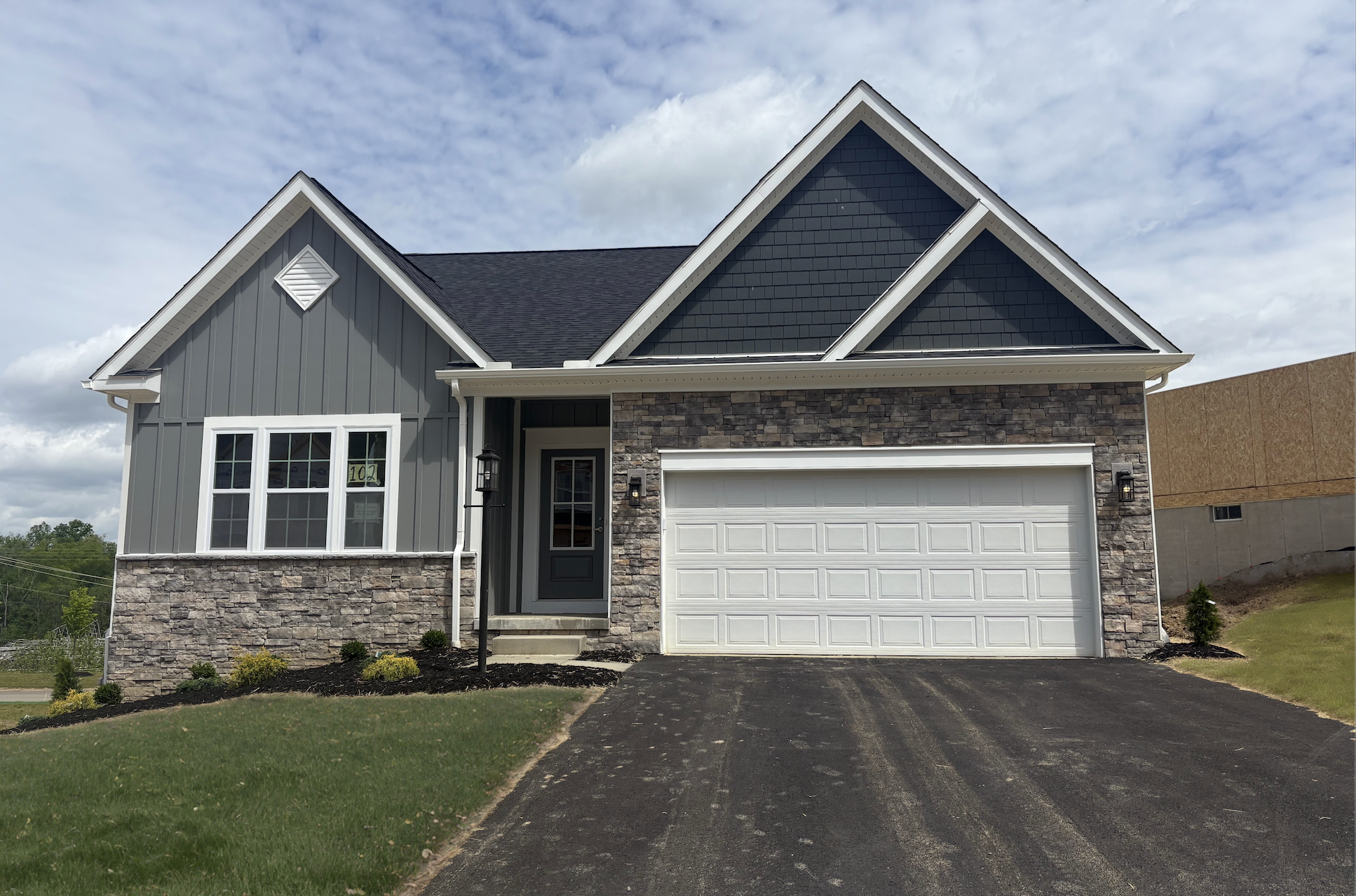 Modern suburban house with a gray exterior, stone accents, and a double garage on a sunny day.