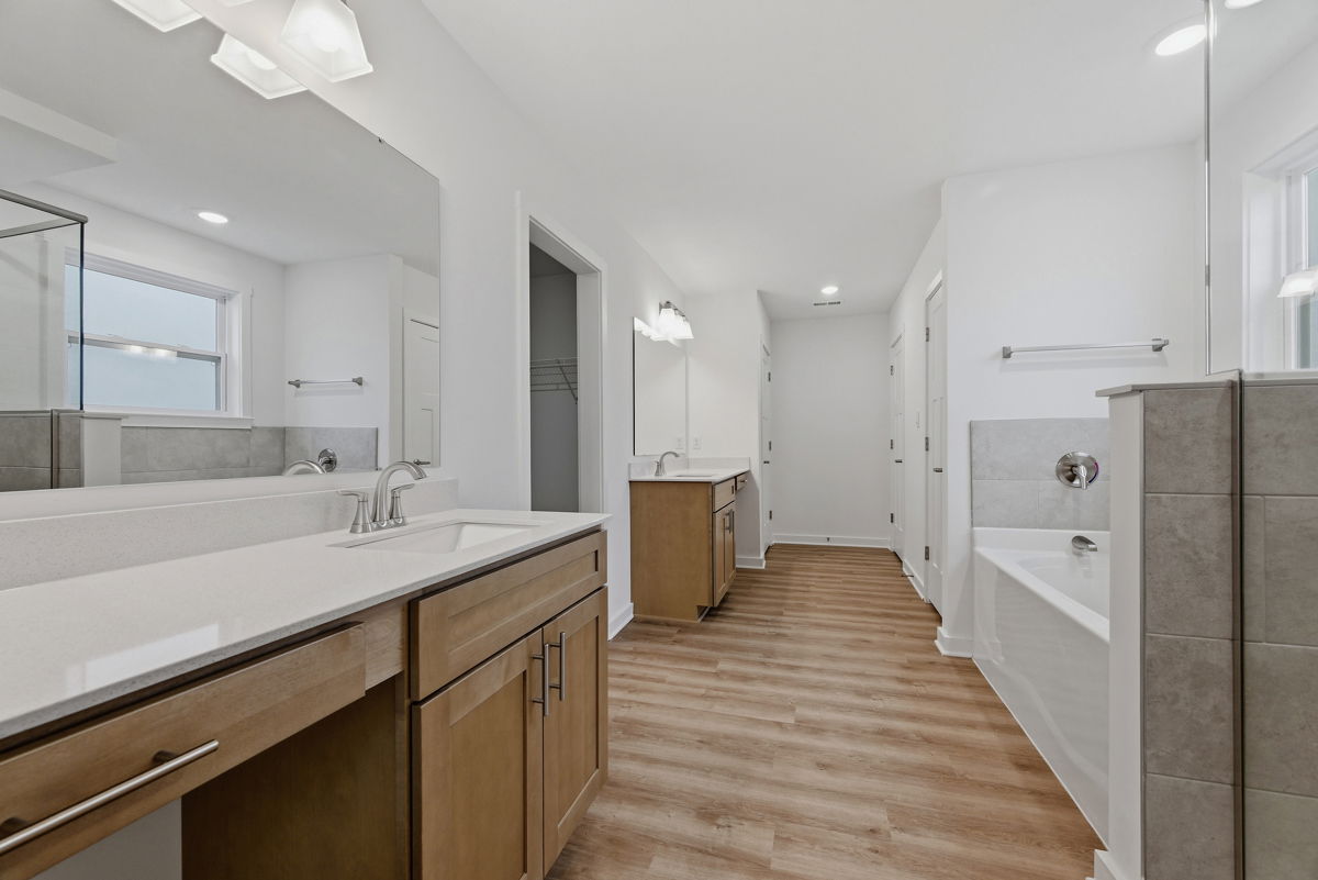 Modern bathroom with double sinks, wooden cabinets, and a bathtub featuring sleek design and wood-look flooring.