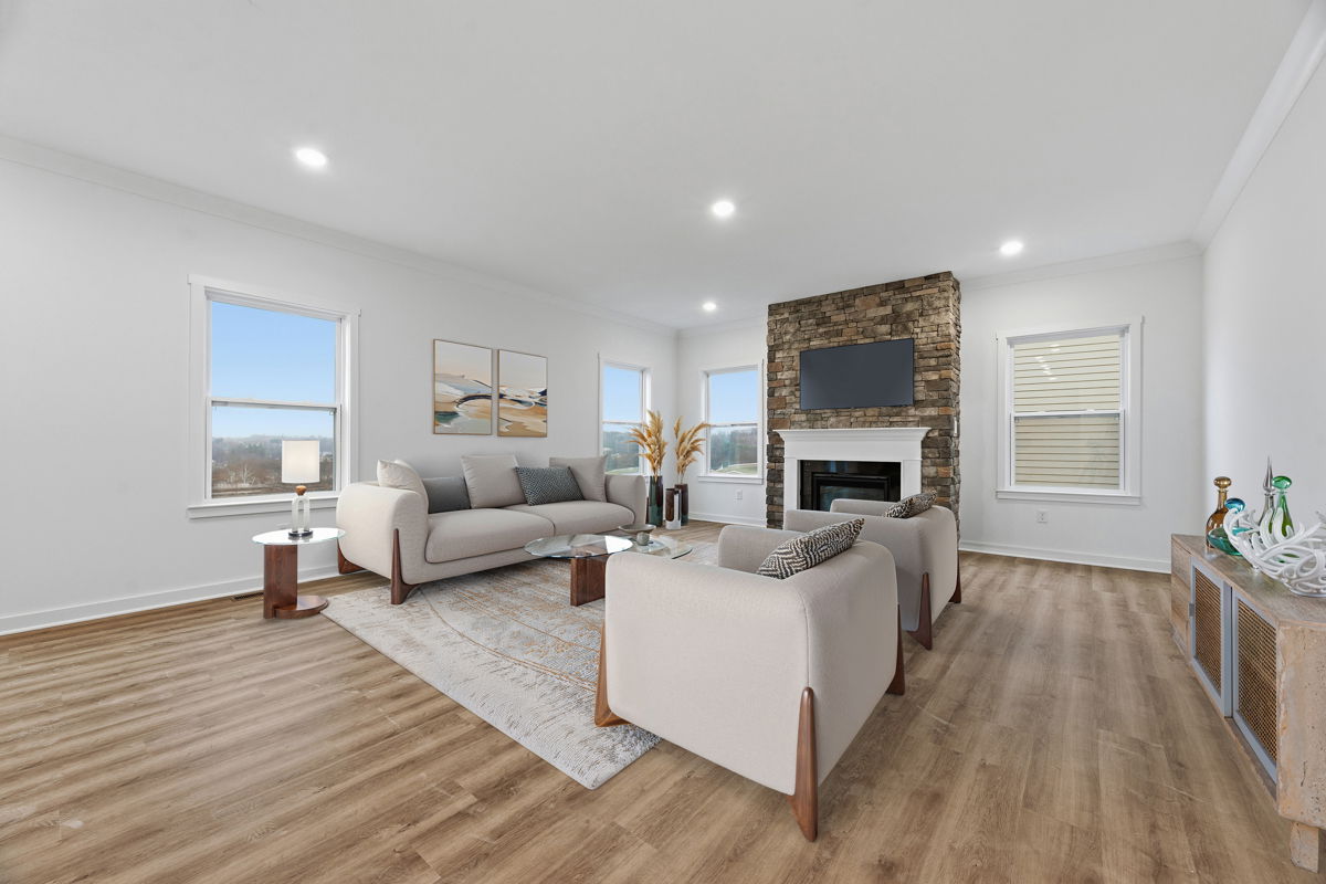 Modern living room with light gray sofas, wooden flooring, a stone fireplace, and large windows.