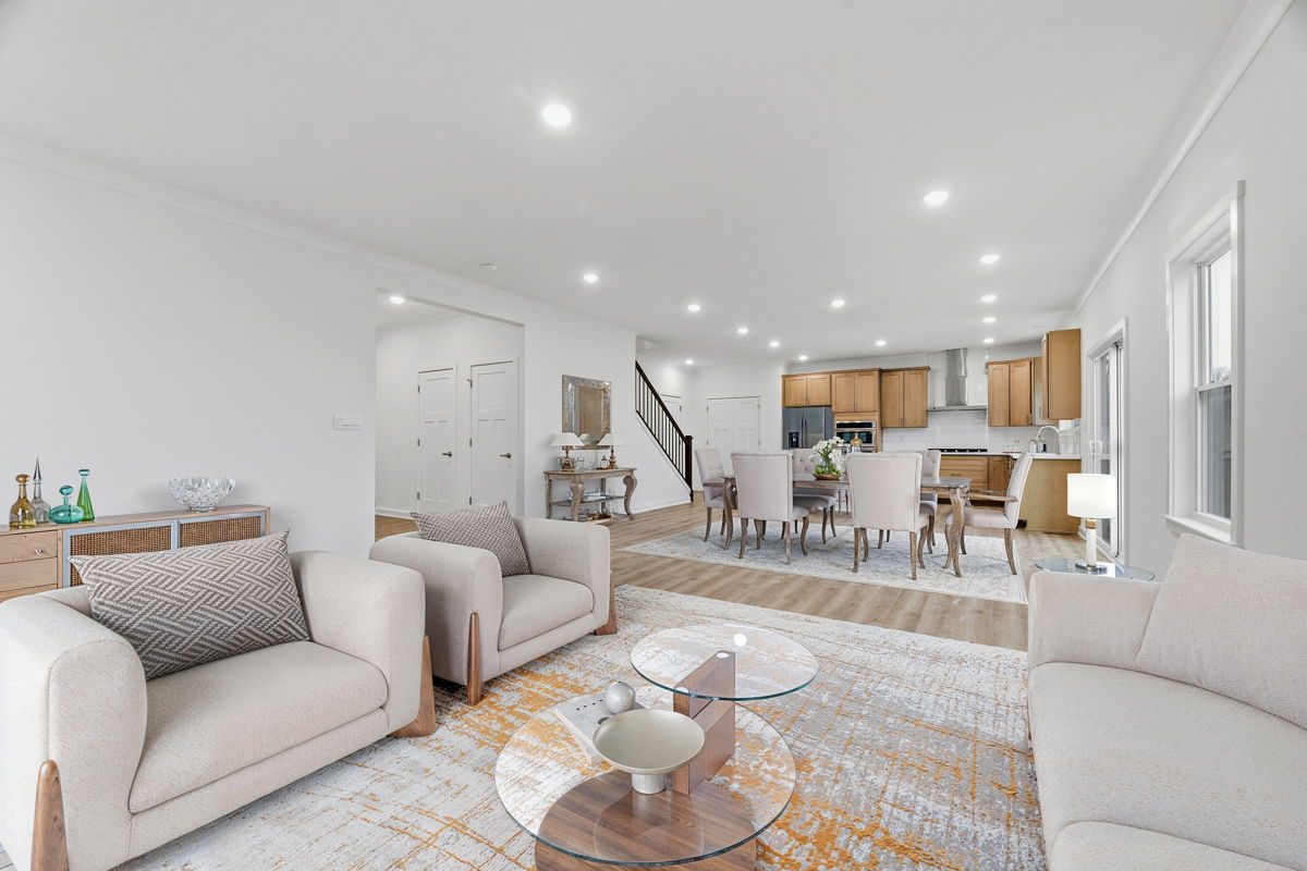 Modern open-concept living and dining room with beige sofas, glass coffee table, and wooden kitchen cabinetry.