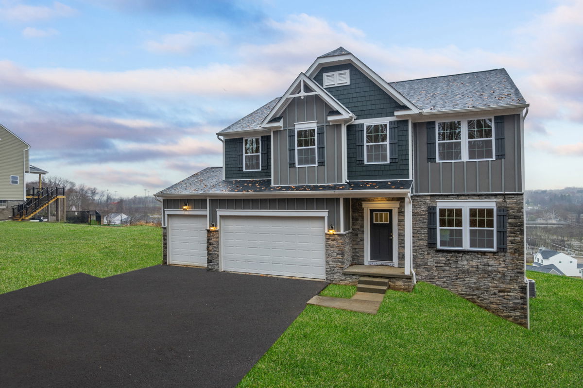 Two-story suburban home with a three-car garage, stone accents, and a manicured lawn under a cloudy sky.