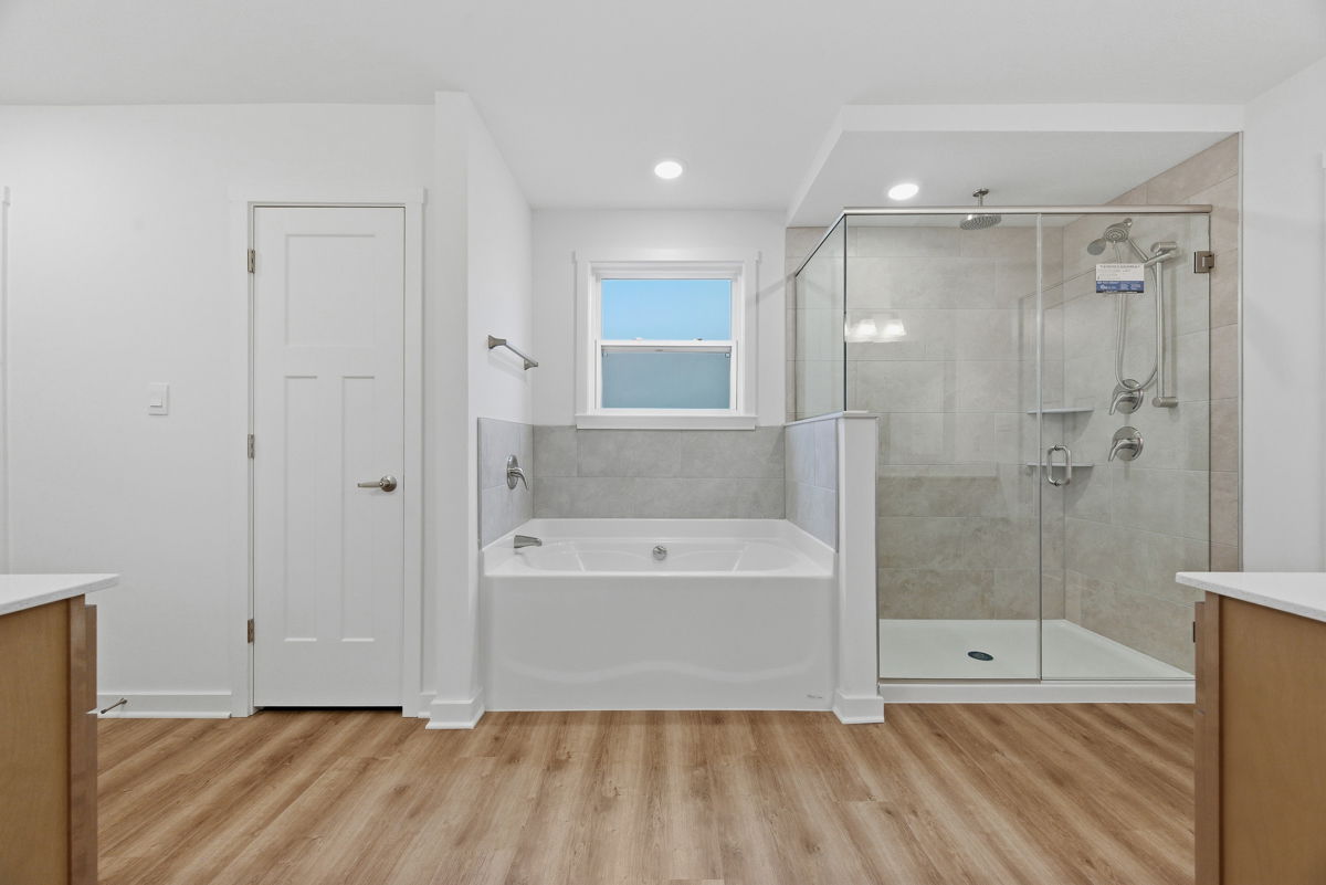 Modern bathroom featuring a glass-enclosed shower, built-in bathtub, and wood-like flooring.