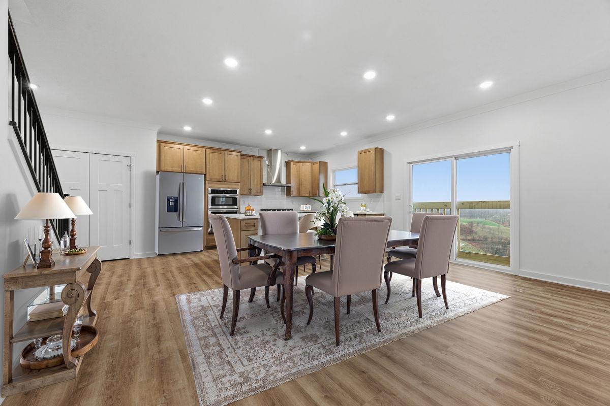 Open-concept kitchen and dining area with wooden flooring, light wood cabinets, and a dining table with beige chairs.