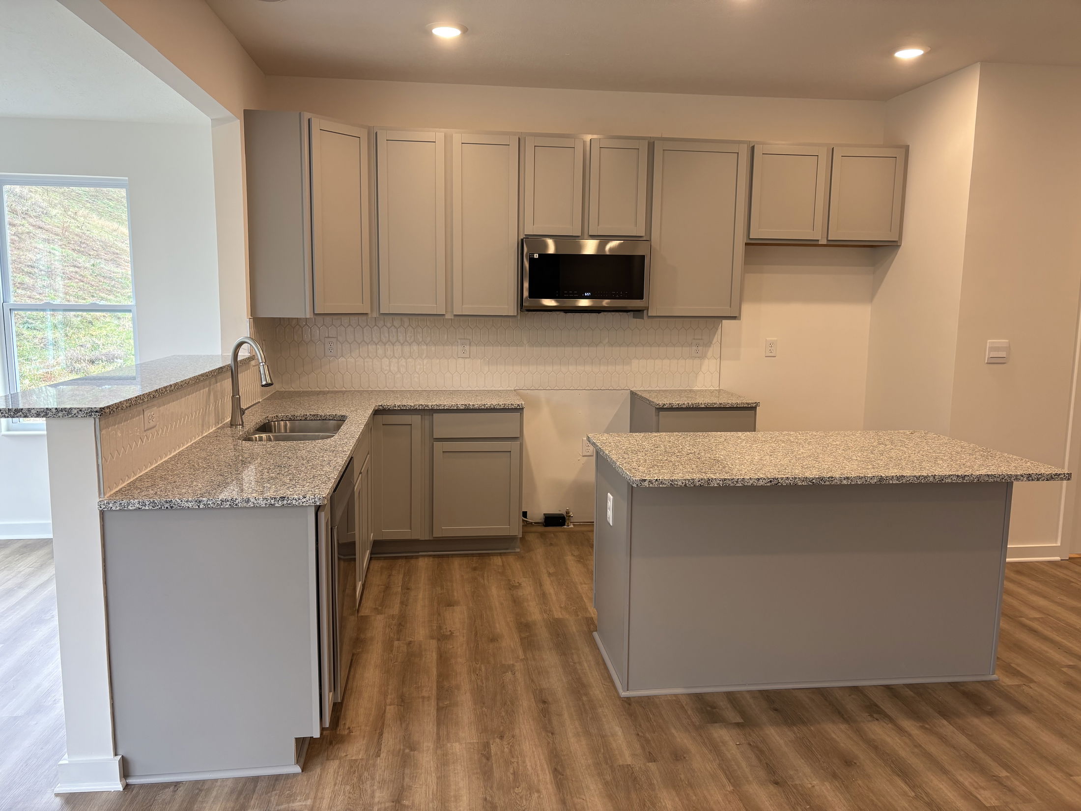 Modern kitchen with gray cabinets, granite countertops, wood flooring, and stainless steel appliances.