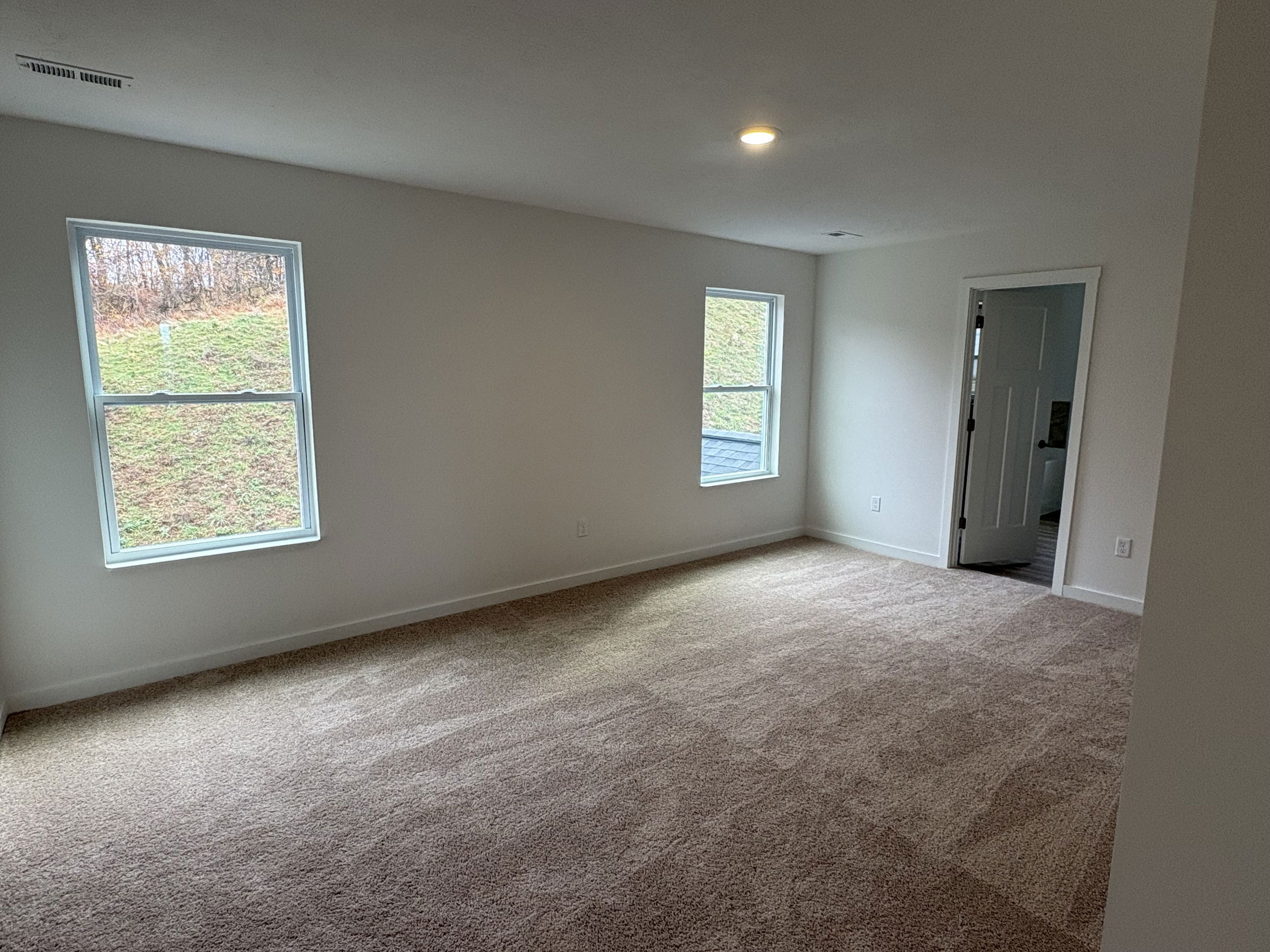 Spacious, carpeted empty room with large windows and a doorway leading to another area.