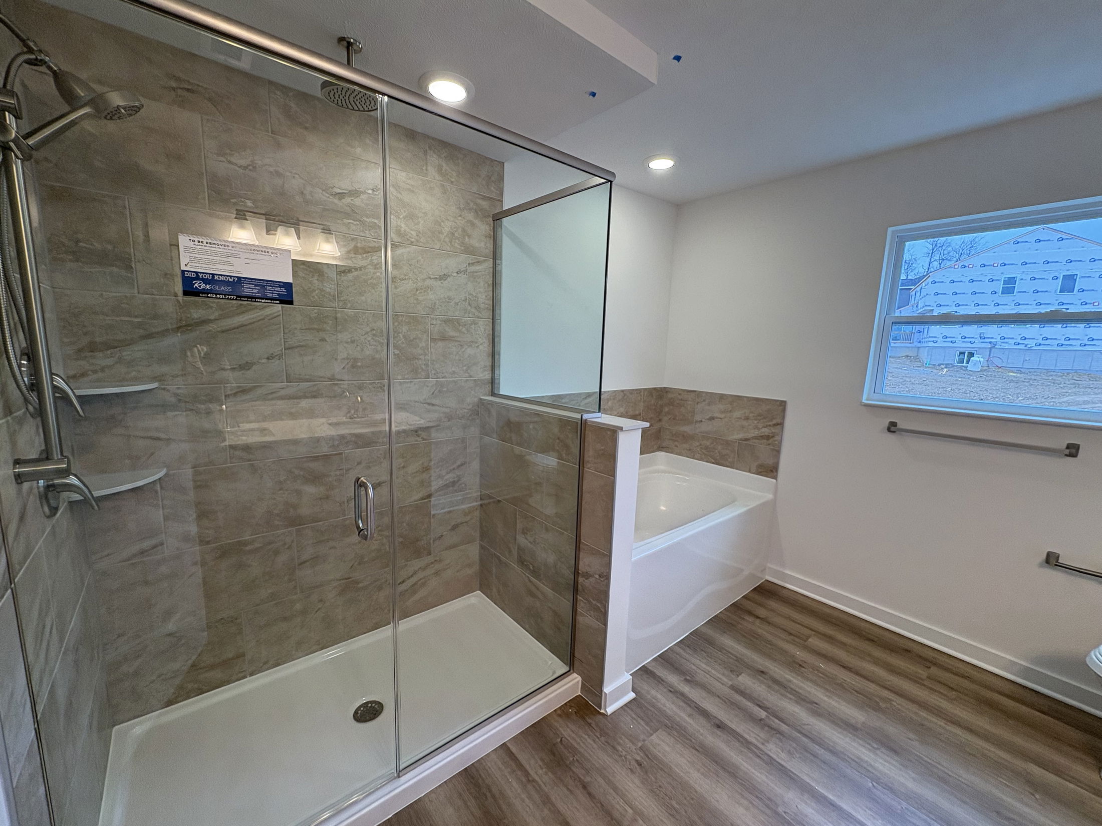 Modern bathroom with a glass-enclosed shower, wooden flooring, and an adjacent bathtub.