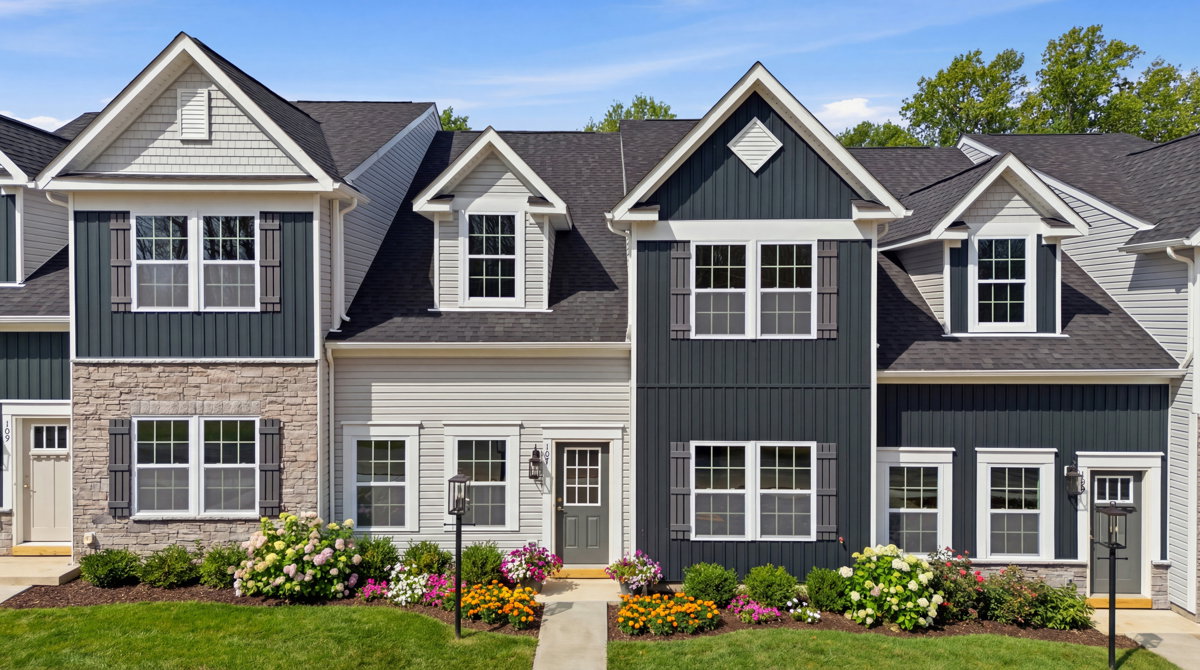 Modern townhouses with a blend of stone and dark siding, surrounded by vibrant flower beds and a clear blue sky.