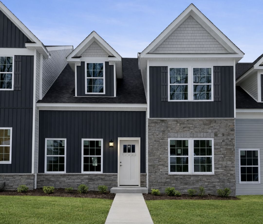 Modern two-story house exterior featuring a mix of dark siding, stone accents, and green landscaping.