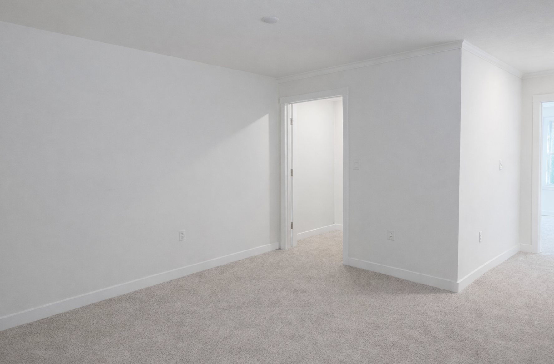 Spacious, empty interior view of a modern room with neutral white walls and soft carpet.