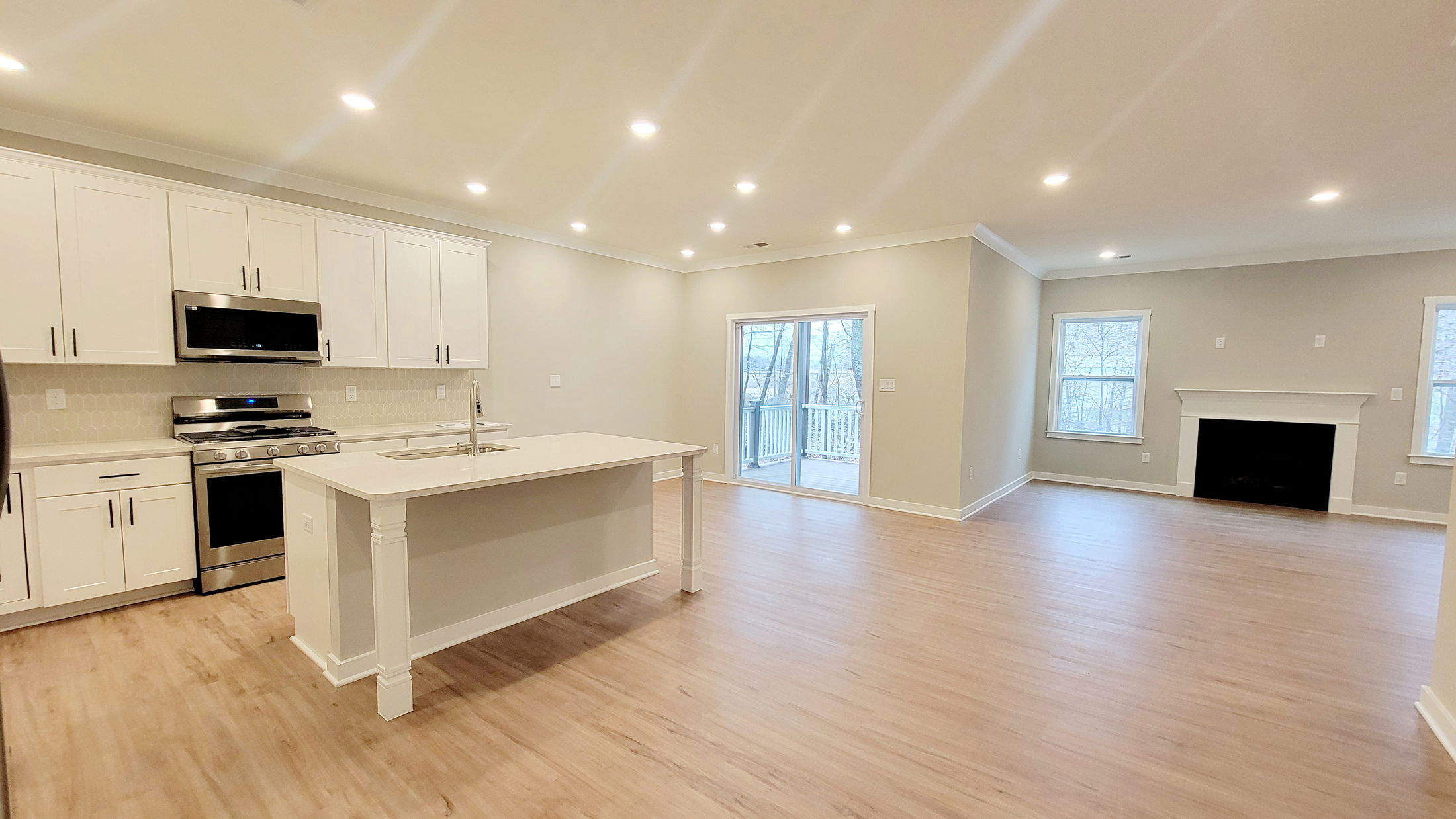 Spacious open-concept kitchen and living room featuring white cabinetry, hardwood floors, and a modern fireplace with large windows.