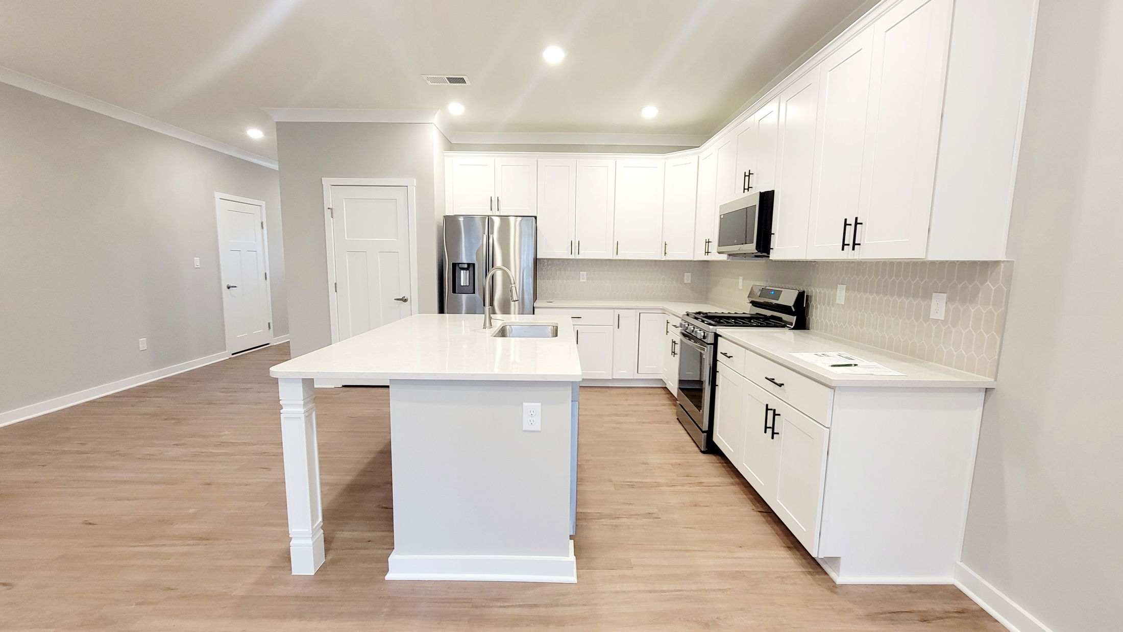 Modern kitchen with white cabinetry, stainless steel appliances, and a central island on hardwood floors.