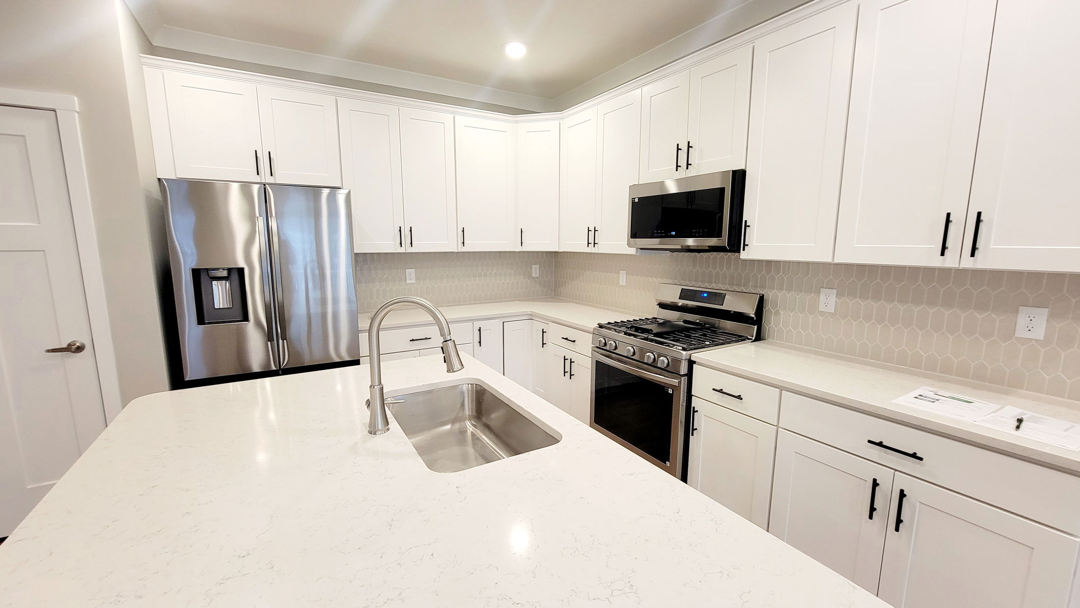 Modern kitchen with white cabinets, stainless steel appliances, and a central island with a sleek faucet and sink.