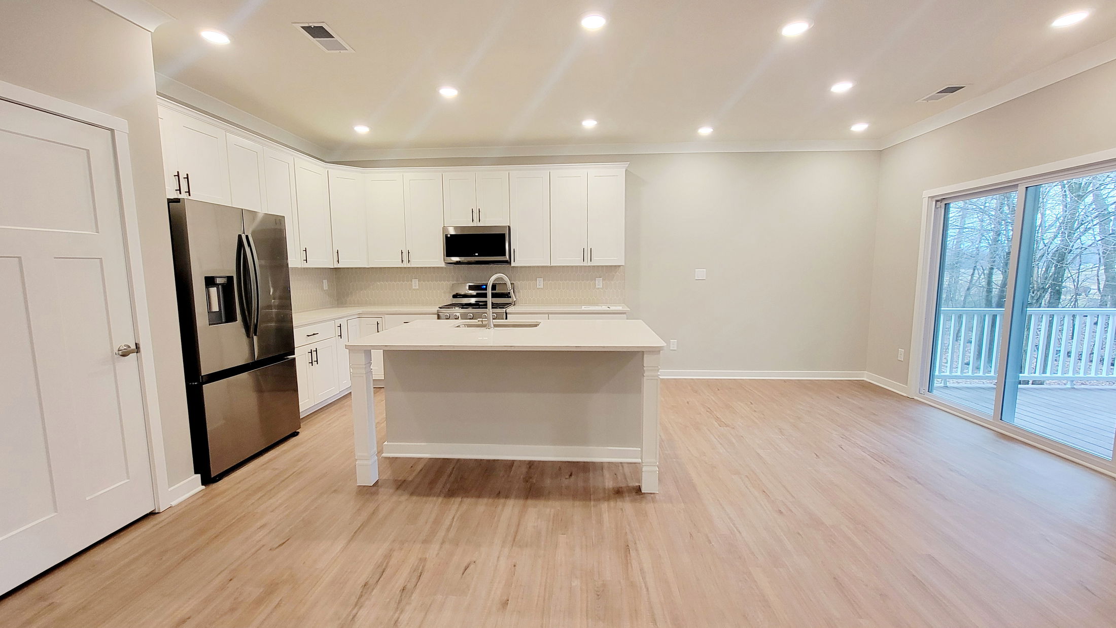 Modern kitchen with white cabinetry, stainless steel appliances, and a wooden floor, adjacent to a sliding glass door leading to a deck.