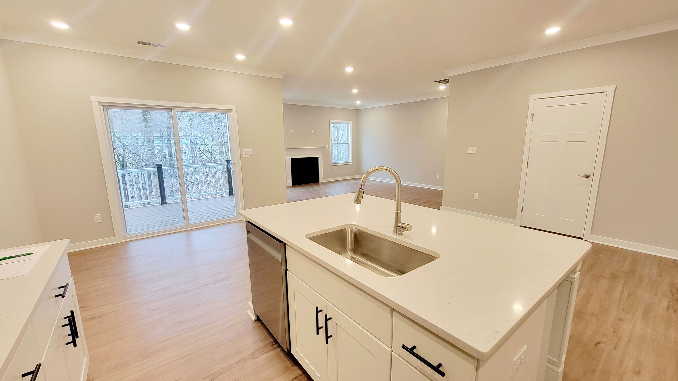 Modern open-concept kitchen and living area with white cabinets, hardwood floors, and sliding glass doors leading to a deck.