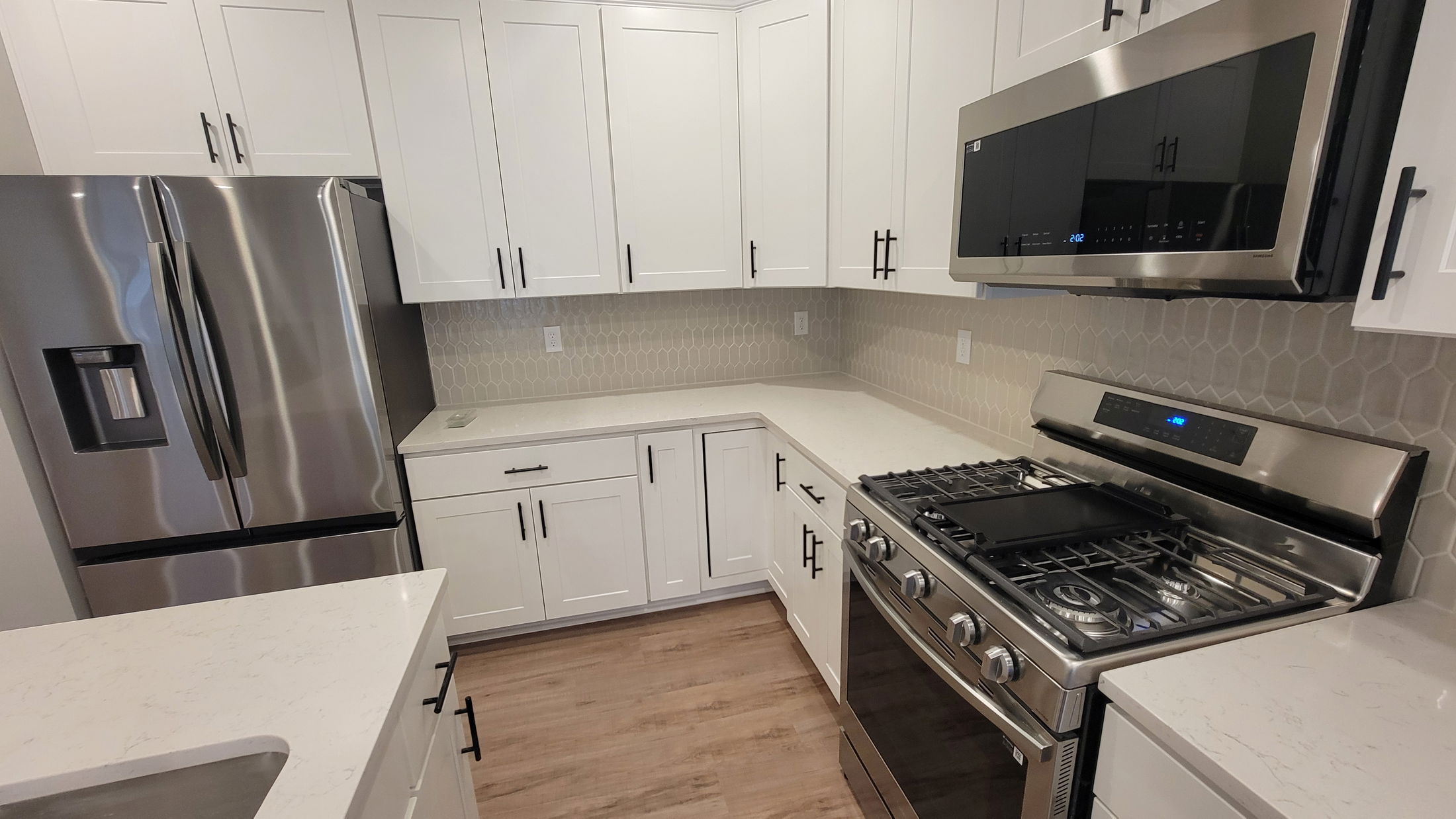 Modern kitchen featuring white shaker cabinets, stainless steel appliances, and a hexagonal tile backsplash.