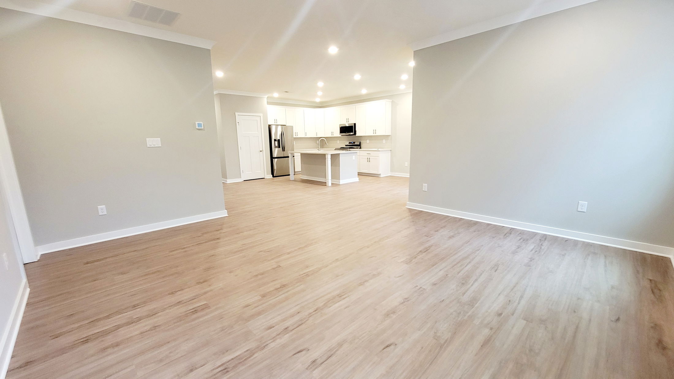 Modern open-plan living room with light wood flooring and spacious white kitchen cabinets.