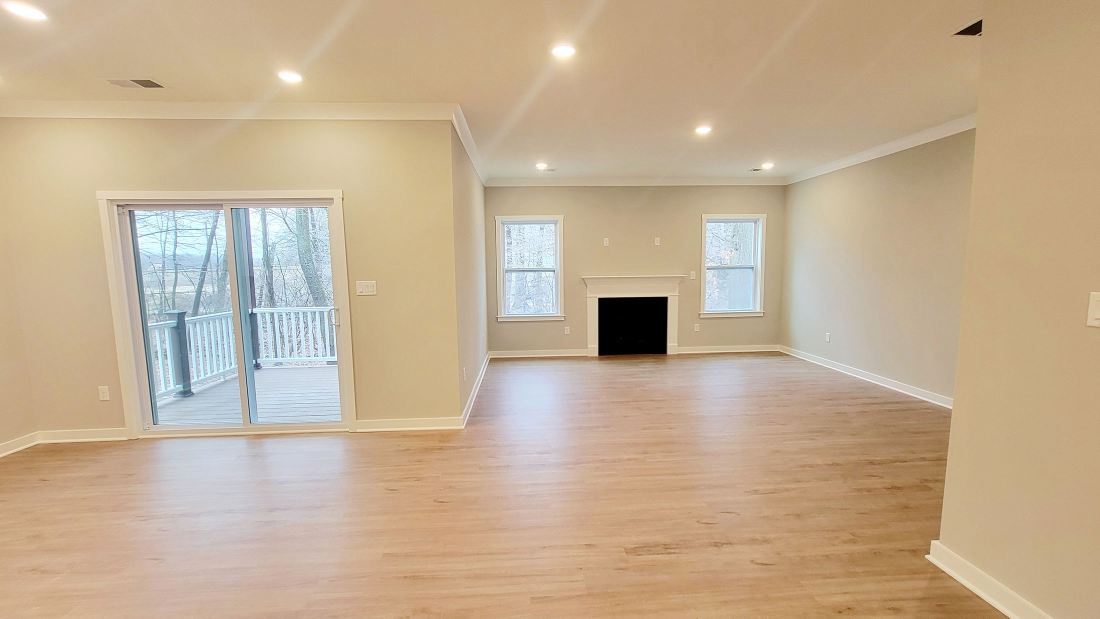 Bright, spacious empty living room with hardwood floors, a fireplace, and sliding glass doors leading to a deck.