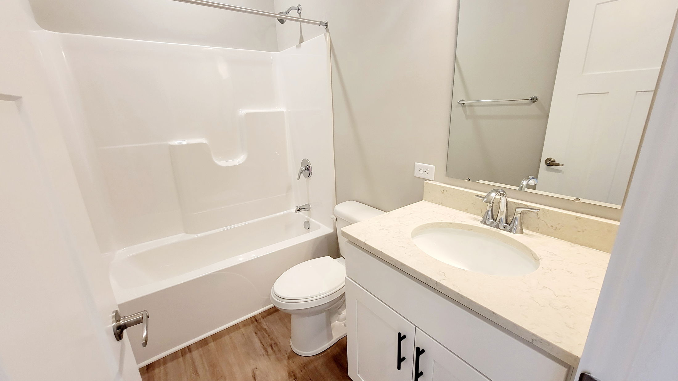 Modern bathroom with white bathtub, toilet, and vanity, featuring wood flooring and a large mirror.