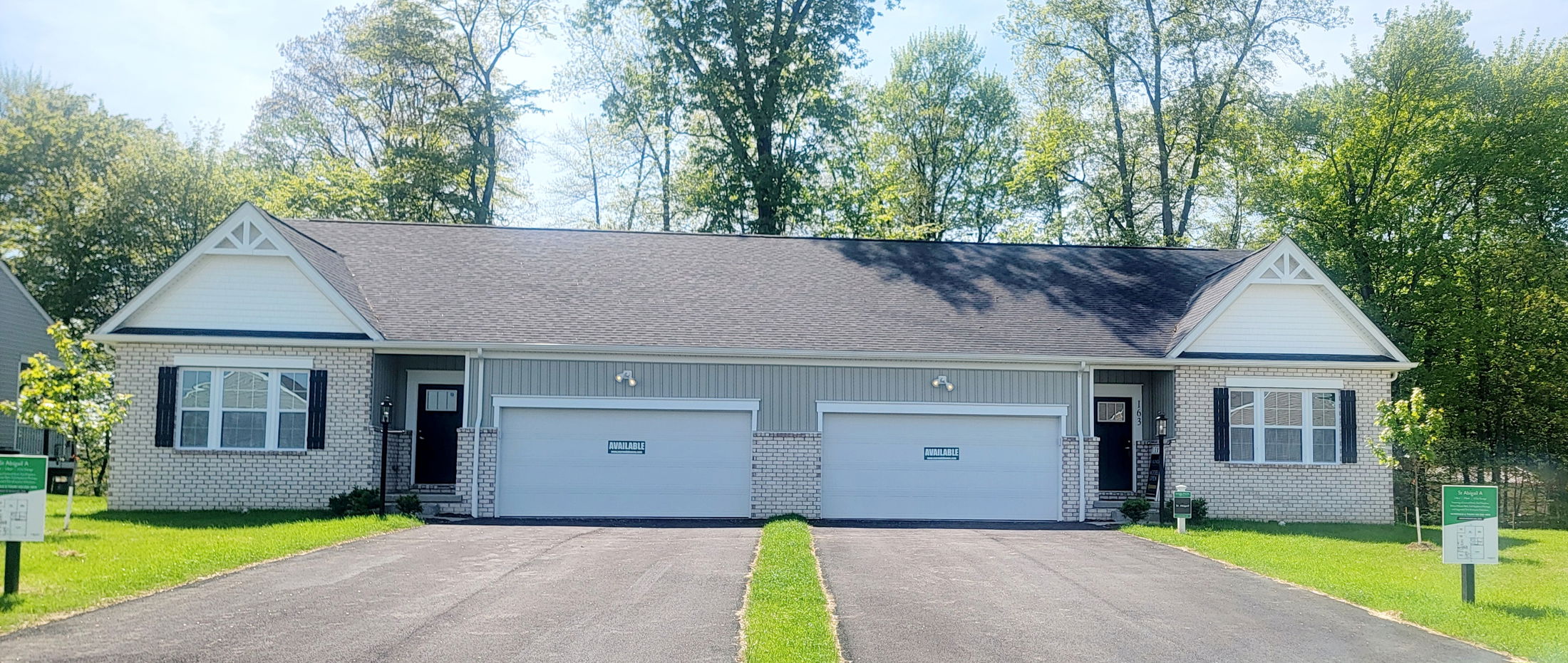 Duplex with brick and siding facade, featuring two garage doors and green 