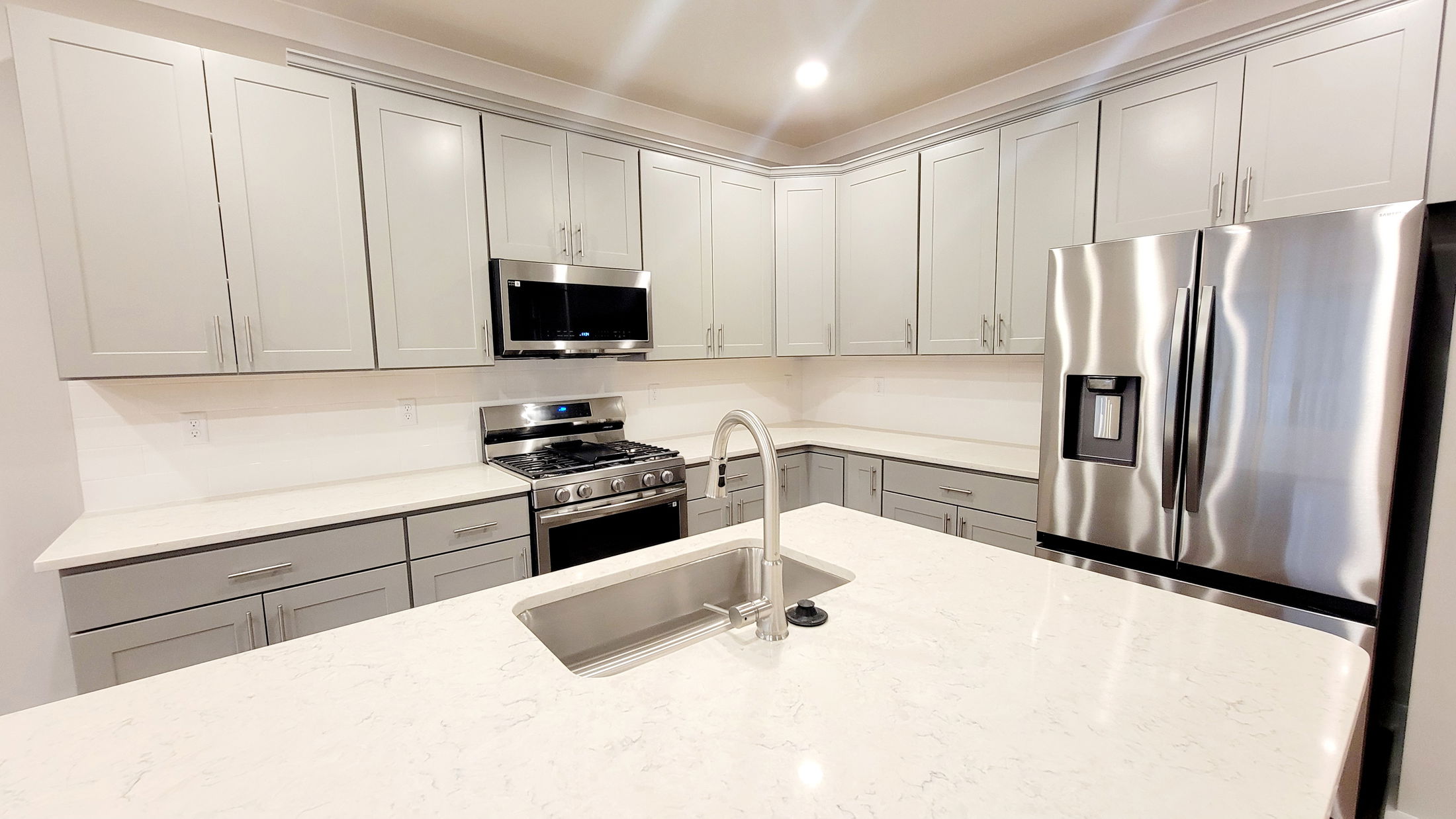 Stylish modern kitchen with stainless steel appliances, white quartz countertops, and gray cabinetry surrounding a central island with a sink.