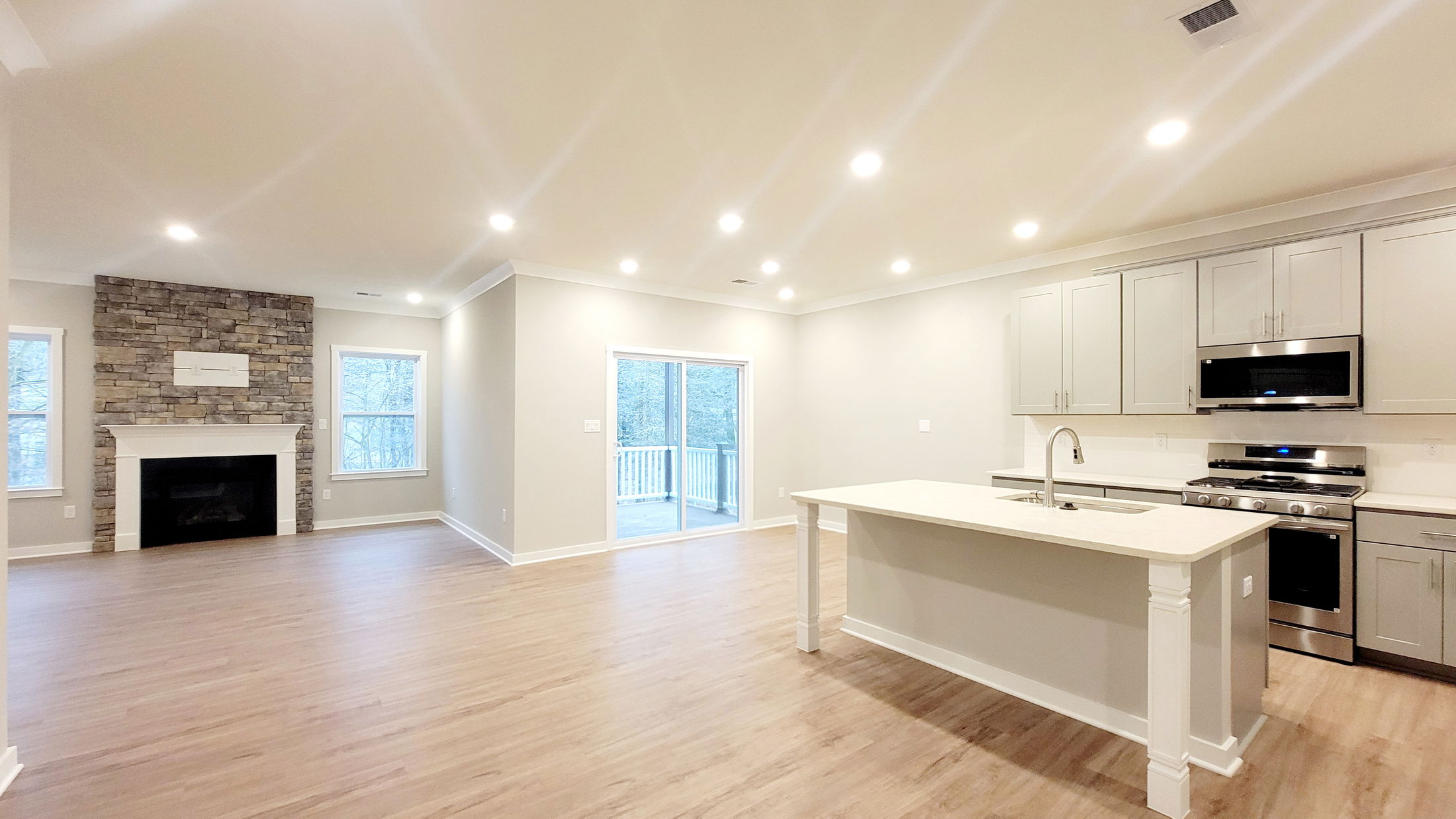 Modern open-concept kitchen and living room with stone fireplace, hardwood flooring, and stainless steel appliances.