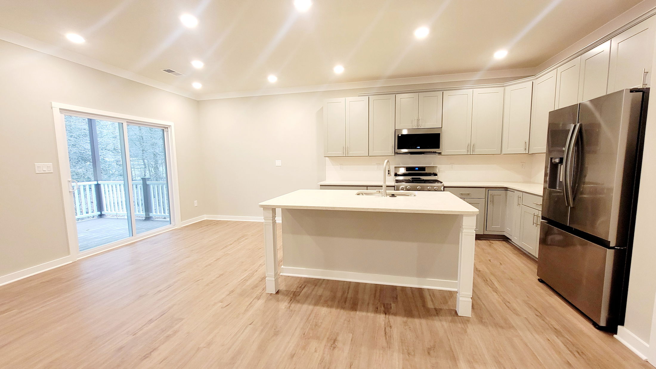 Modern kitchen with stainless steel appliances, white cabinets, and a central island, featuring a hardwood floor and sliding glass doors.