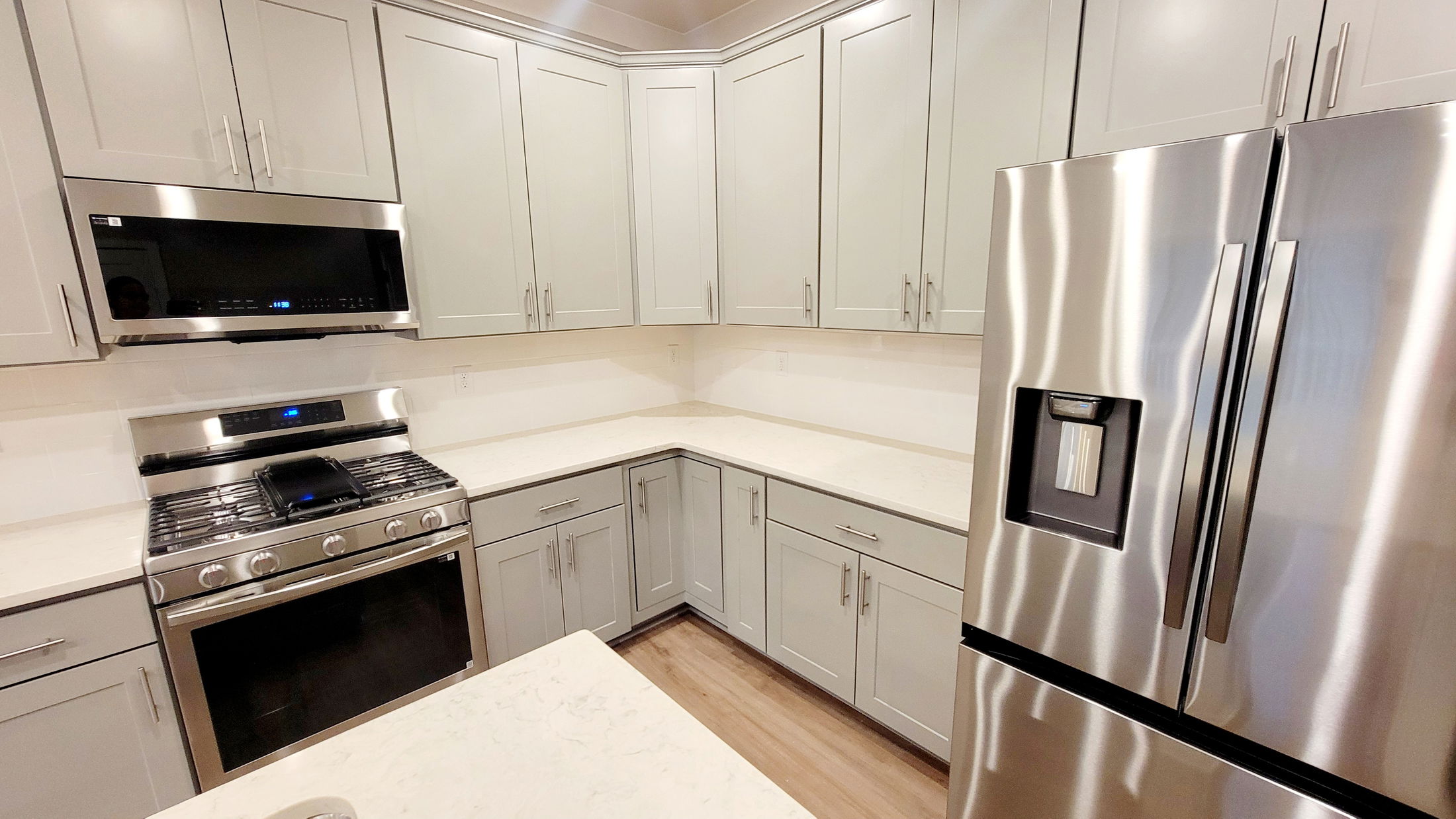 Modern kitchen with stainless steel appliances, white cabinetry, and wooden flooring.