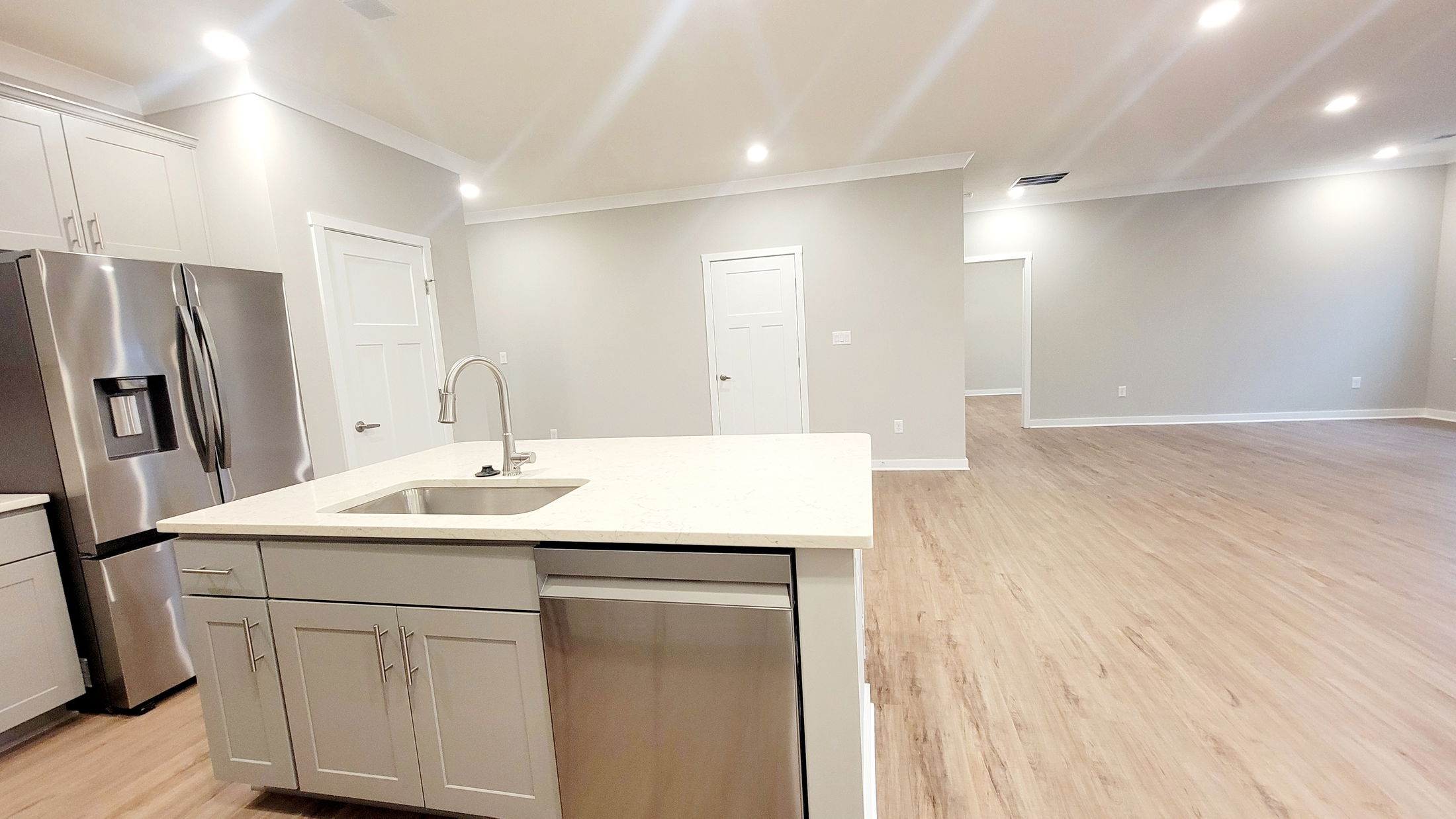 Modern open-concept kitchen and living space featuring light wood flooring, white cabinets, stainless steel appliances, and recessed lighting.