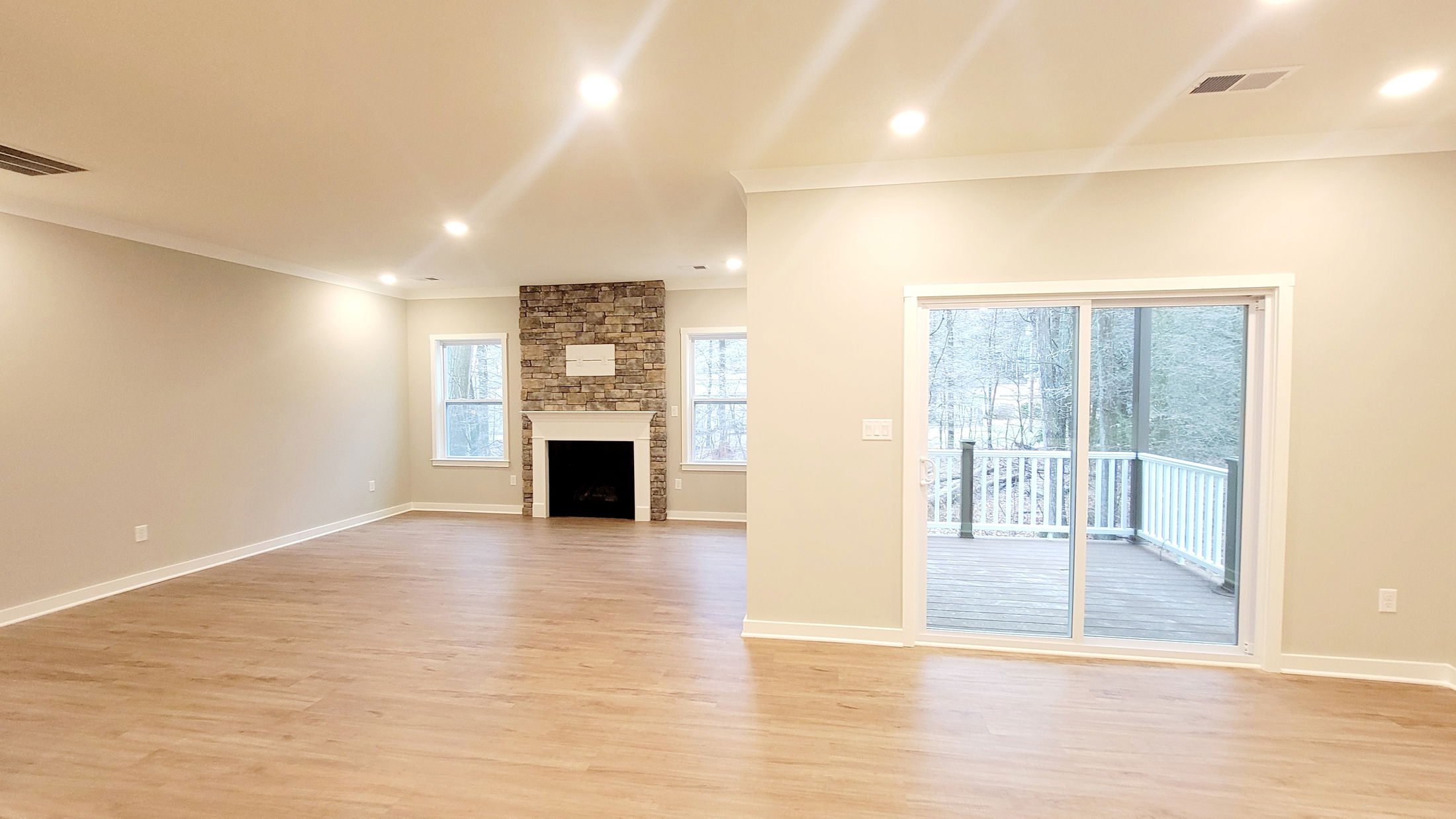 Spacious living room with hardwood floors, a stone fireplace, and sliding glass doors leading to a deck with forest views.