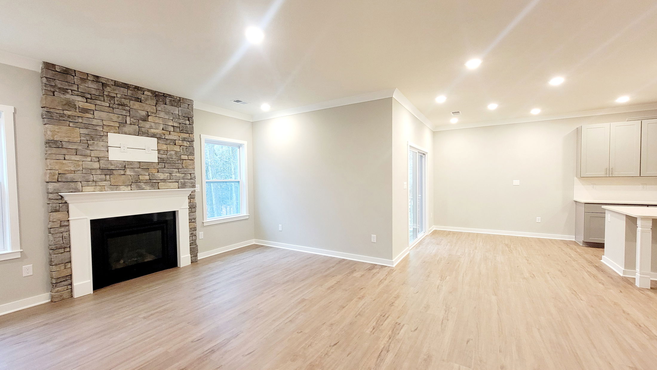 Bright, modern open living space with a stone fireplace, hardwood flooring, and recessed lighting.