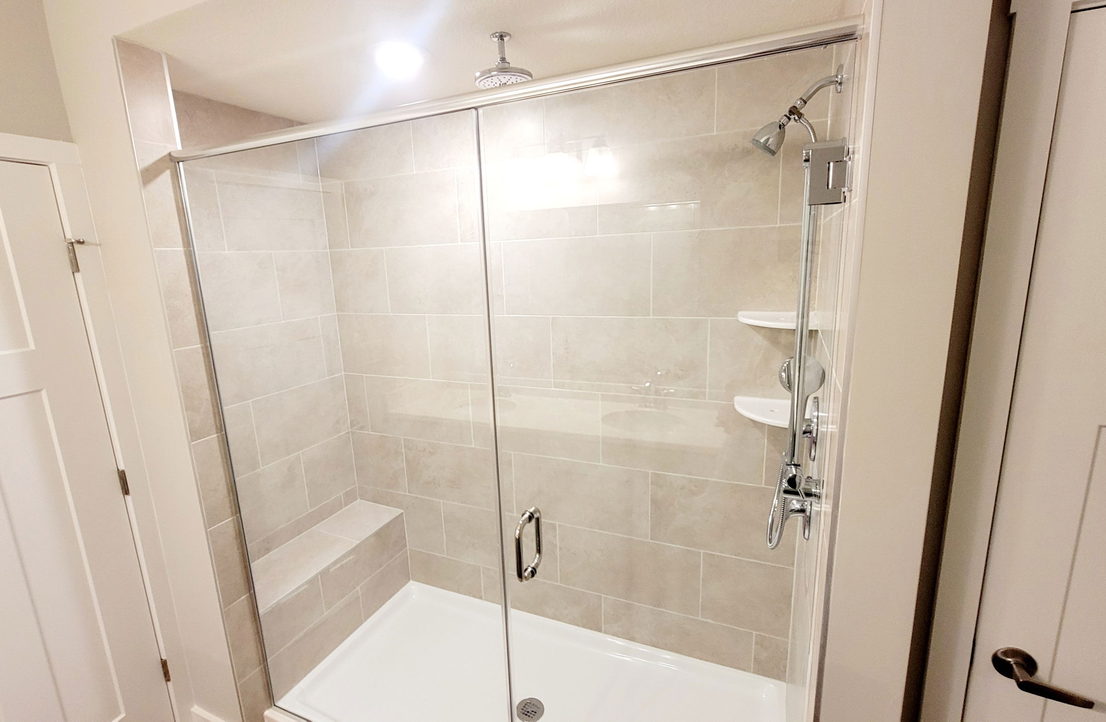 Modern bathroom shower with glass doors, beige tile walls, and built-in bench.