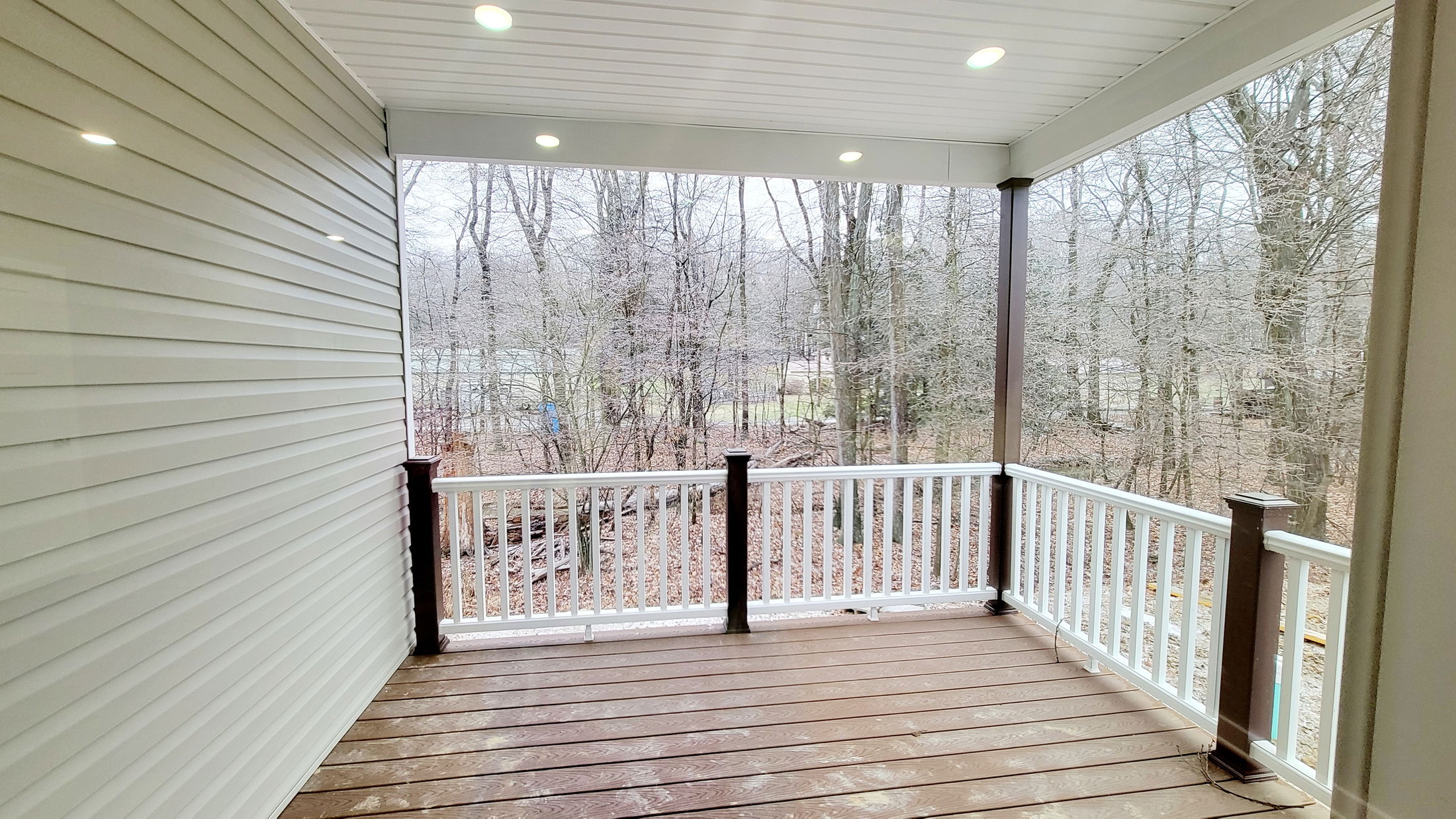 Covered outdoor deck with white railing and wooded view.