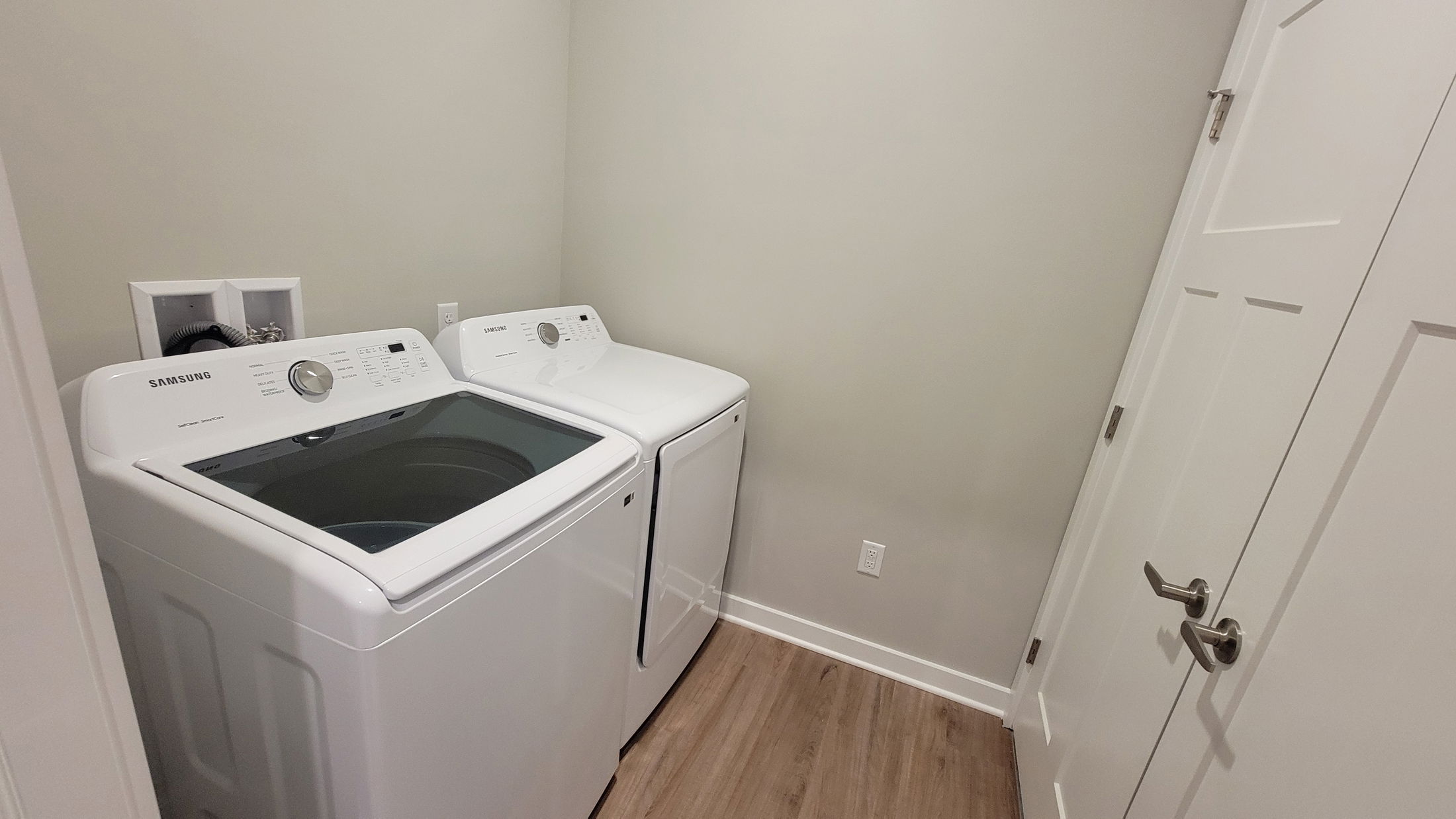 Small laundry room with Samsung washer and dryer on a wooden floor.