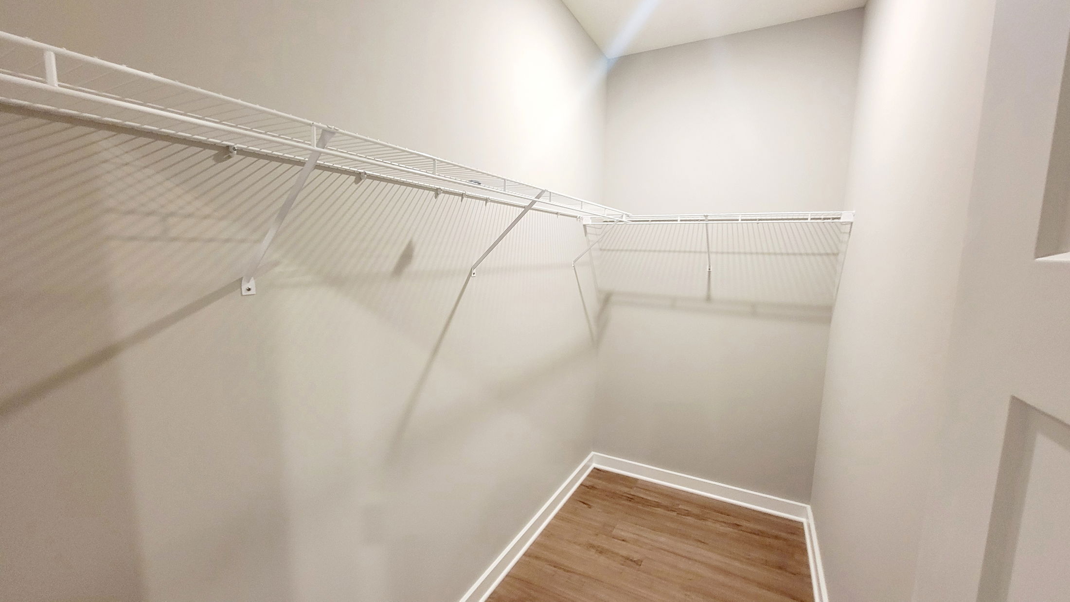 Empty walk-in closet with white wire shelving and hardwood flooring.