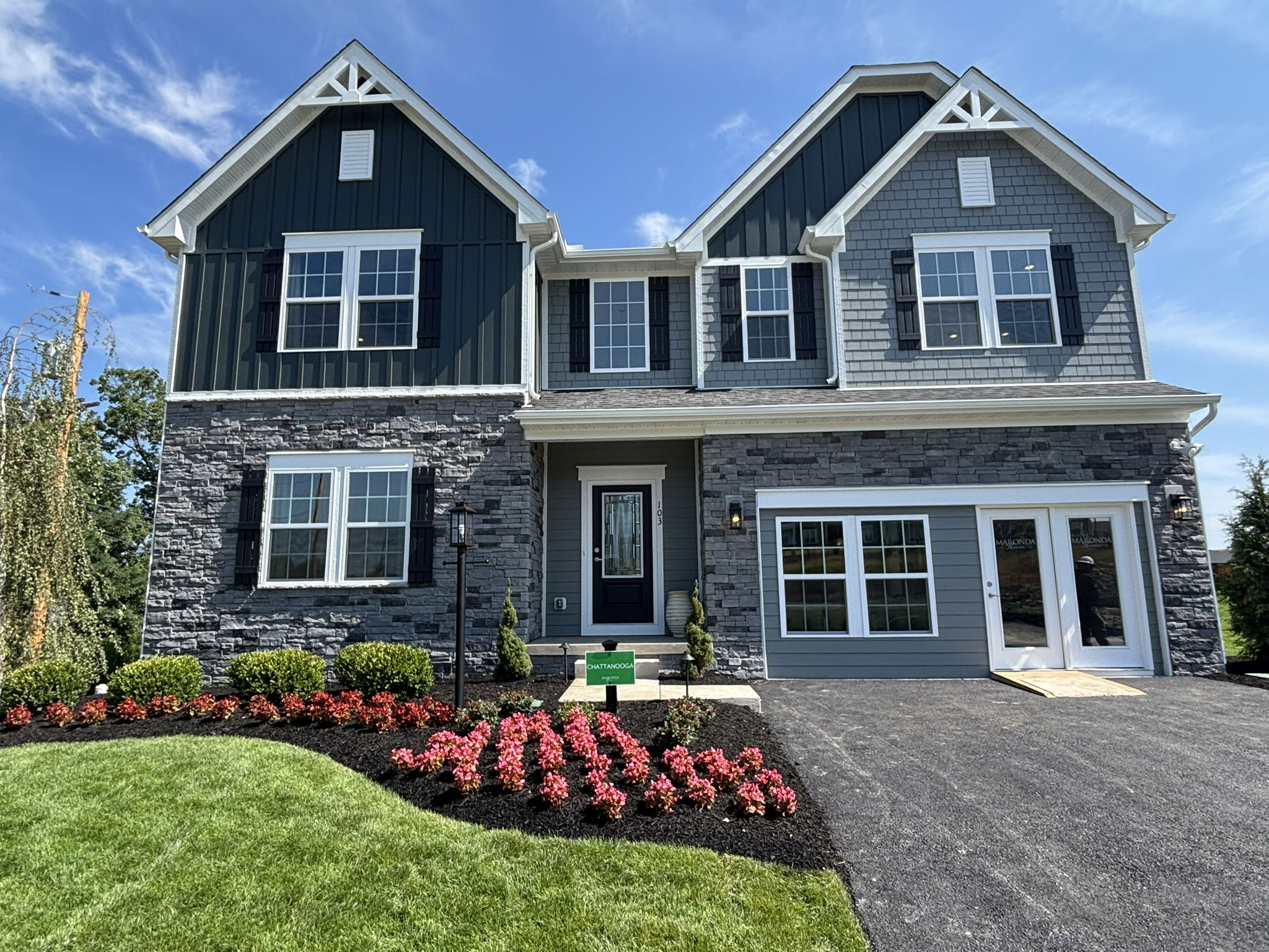 Modern two-story house with gray siding and manicured landscaping under a clear blue sky.