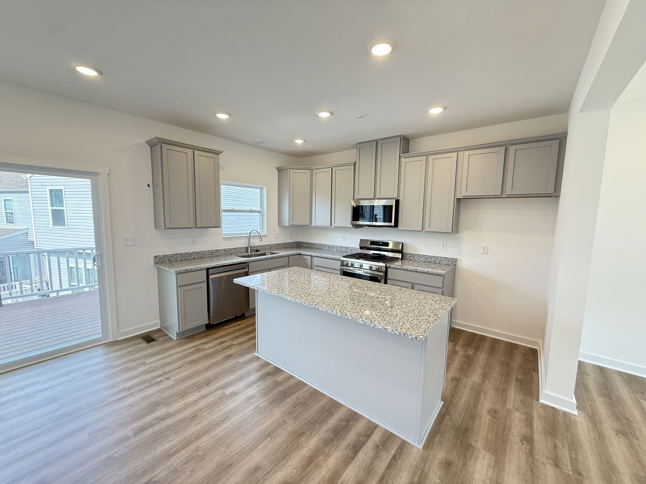 Modern kitchen with granite countertops, stainless steel appliances, gray cabinets, and wood flooring.